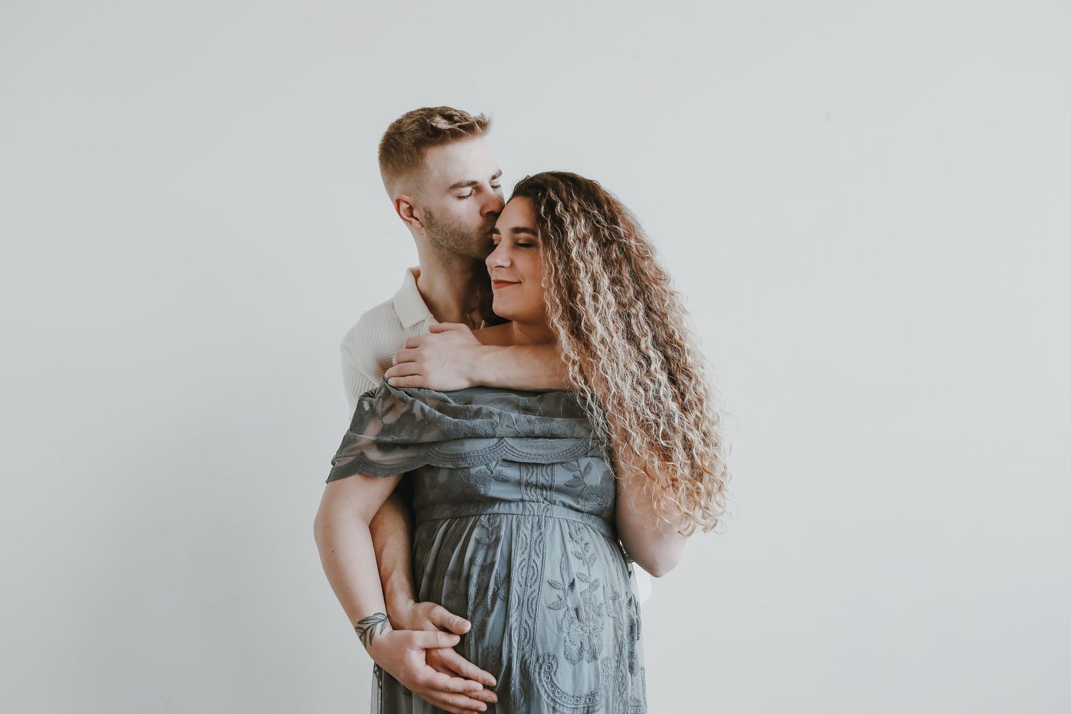 Intimate maternity portrait of couple embracing against white background.