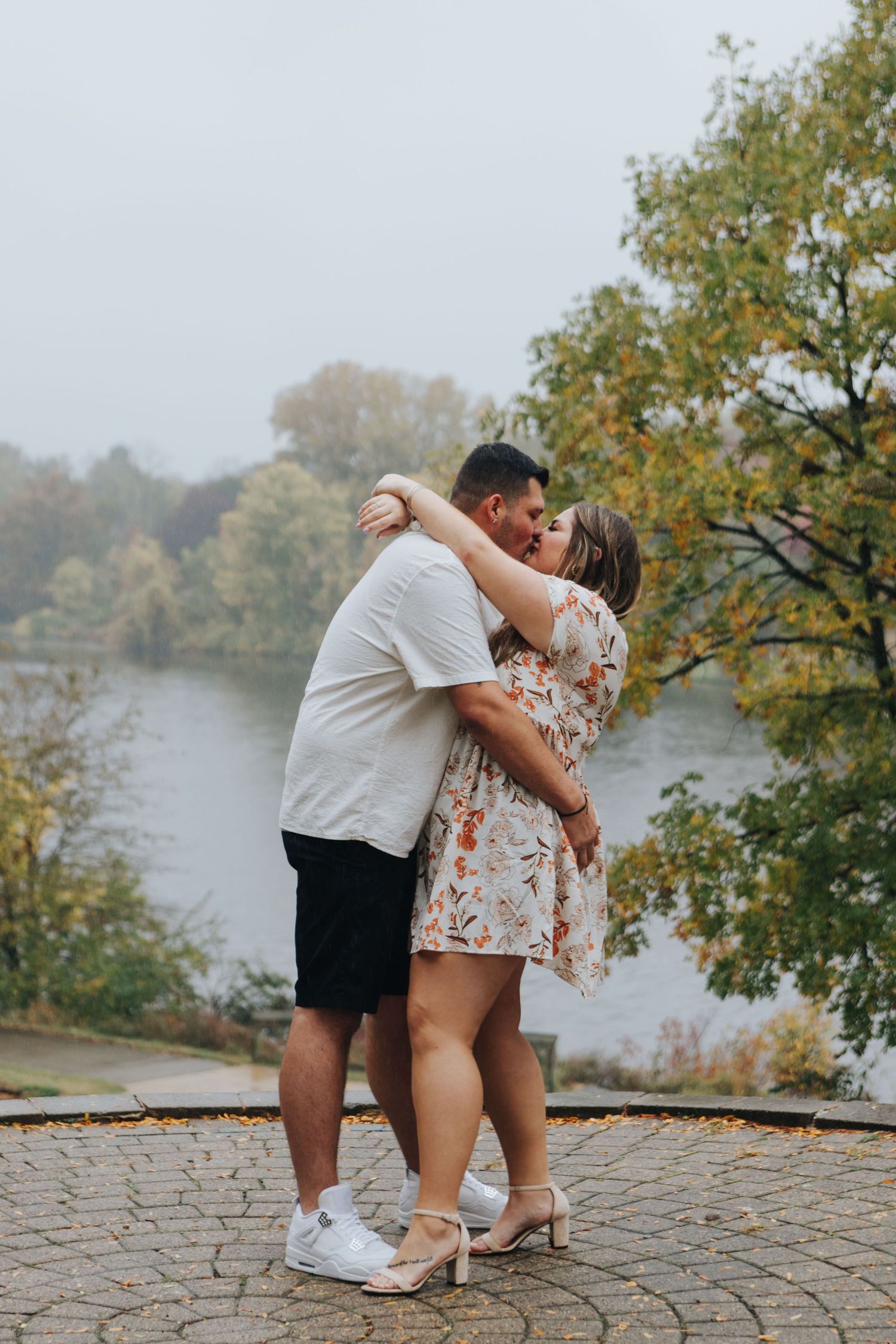 A romantic embrace on a stone patio overlooking a serene lake during autumn.