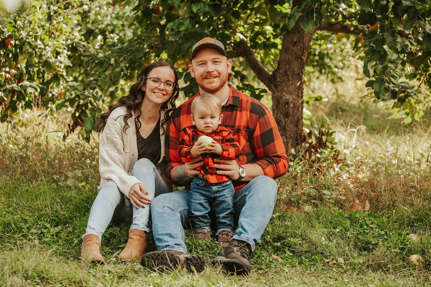A family sits together on fallen autumn leaves in a wooded outdoor setting during a photo session.