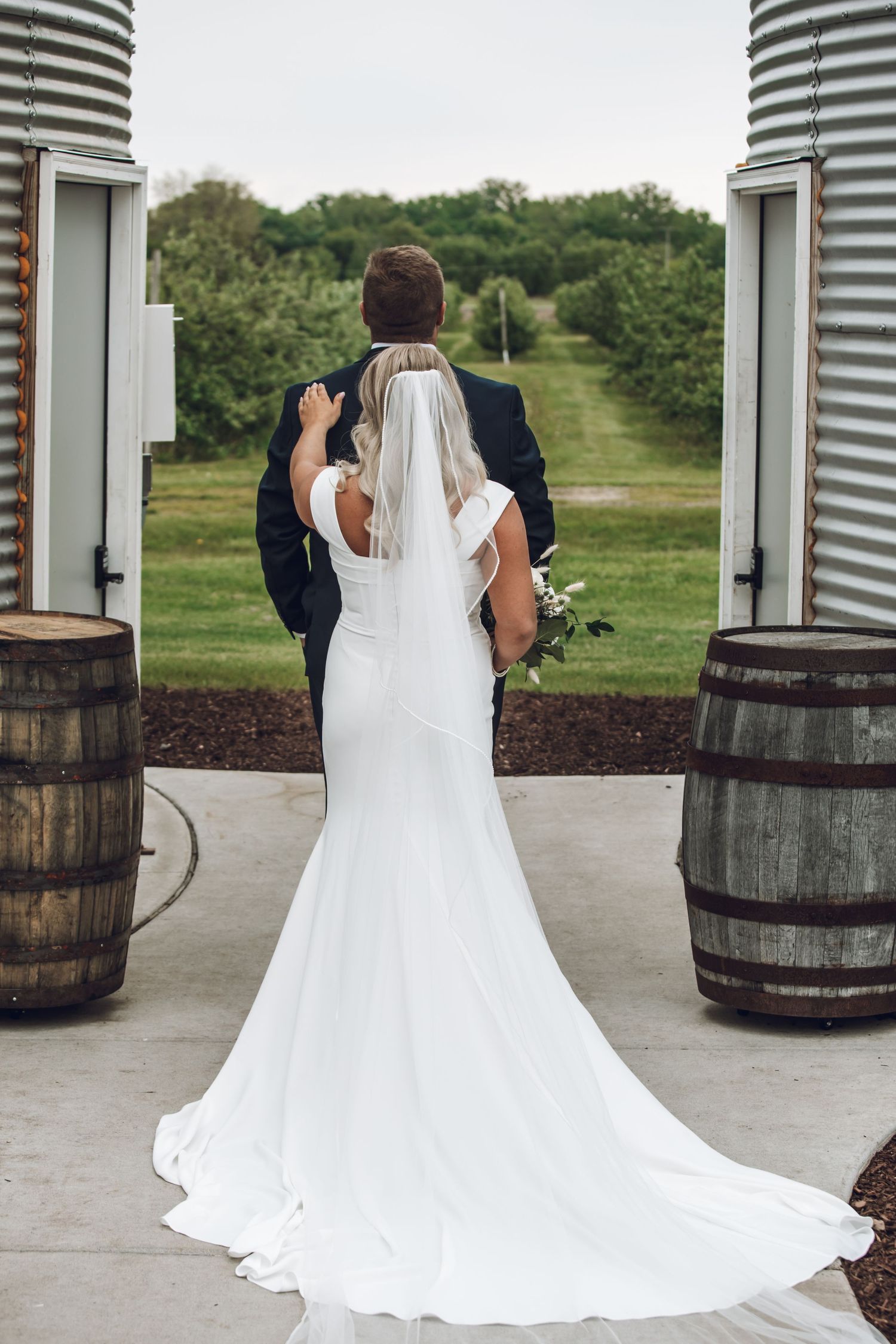 Wedding dress train flowing elegantly across concrete floor with rustic wooden barrels in the background.