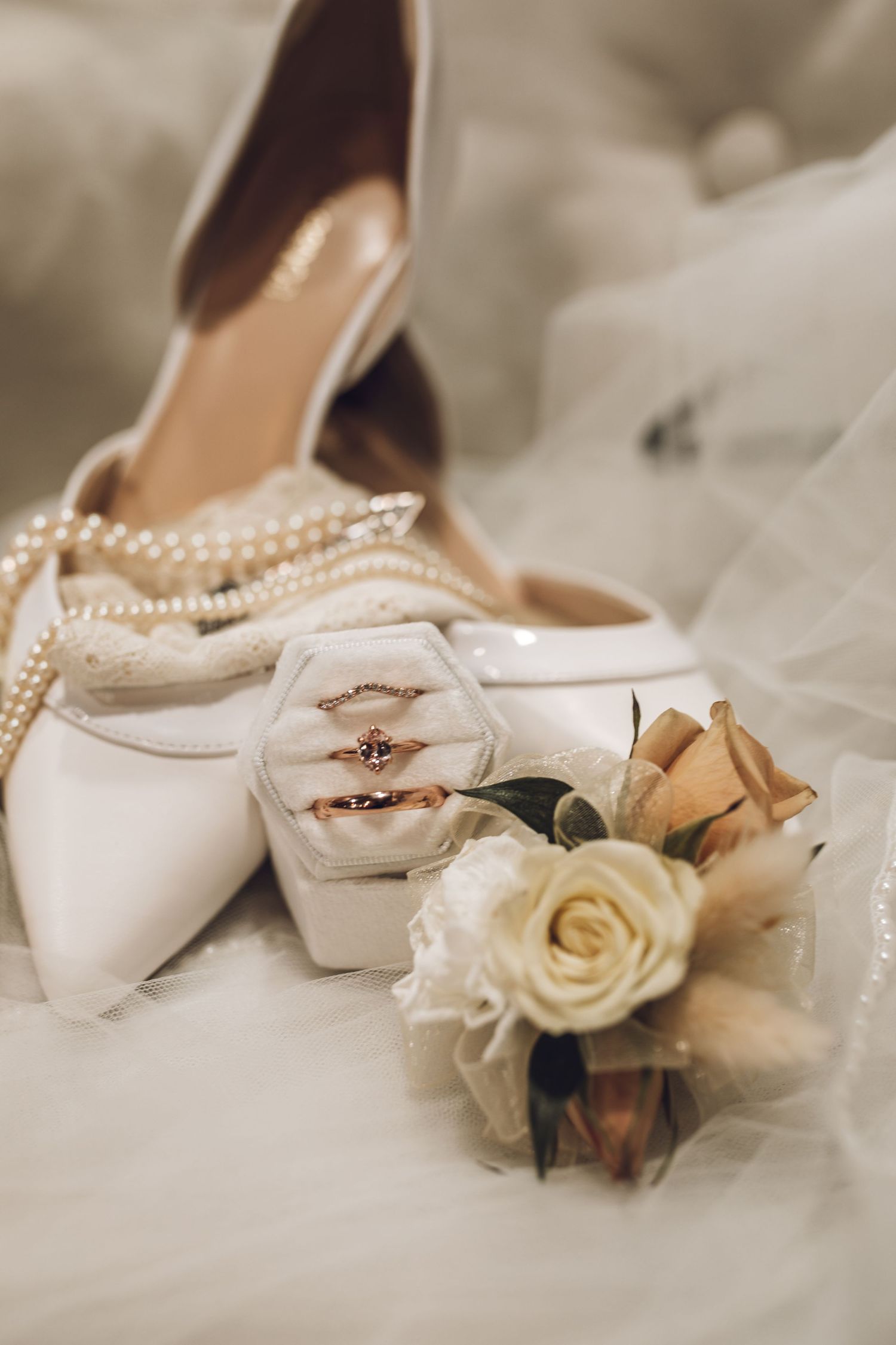 White bridal shoes adorned with delicate pearls and floral decorations rest on tulle fabric.