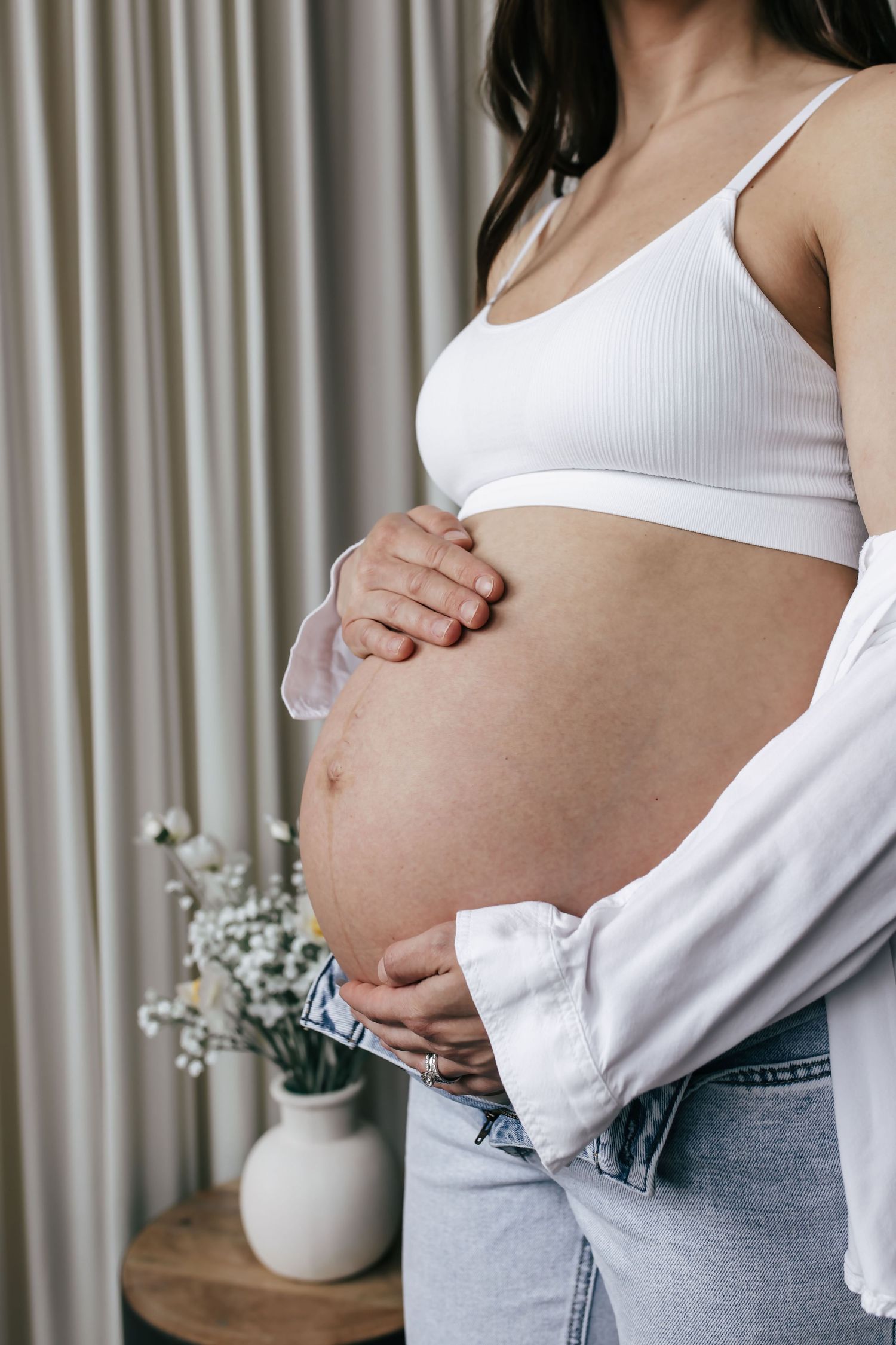 Sequential photos of a growing baby bump in casual white top and jeans against a light curtain.