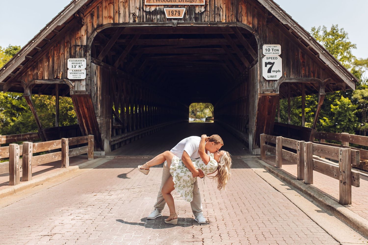 A romantic dip pose in front of a rustic covered wooden bridge.