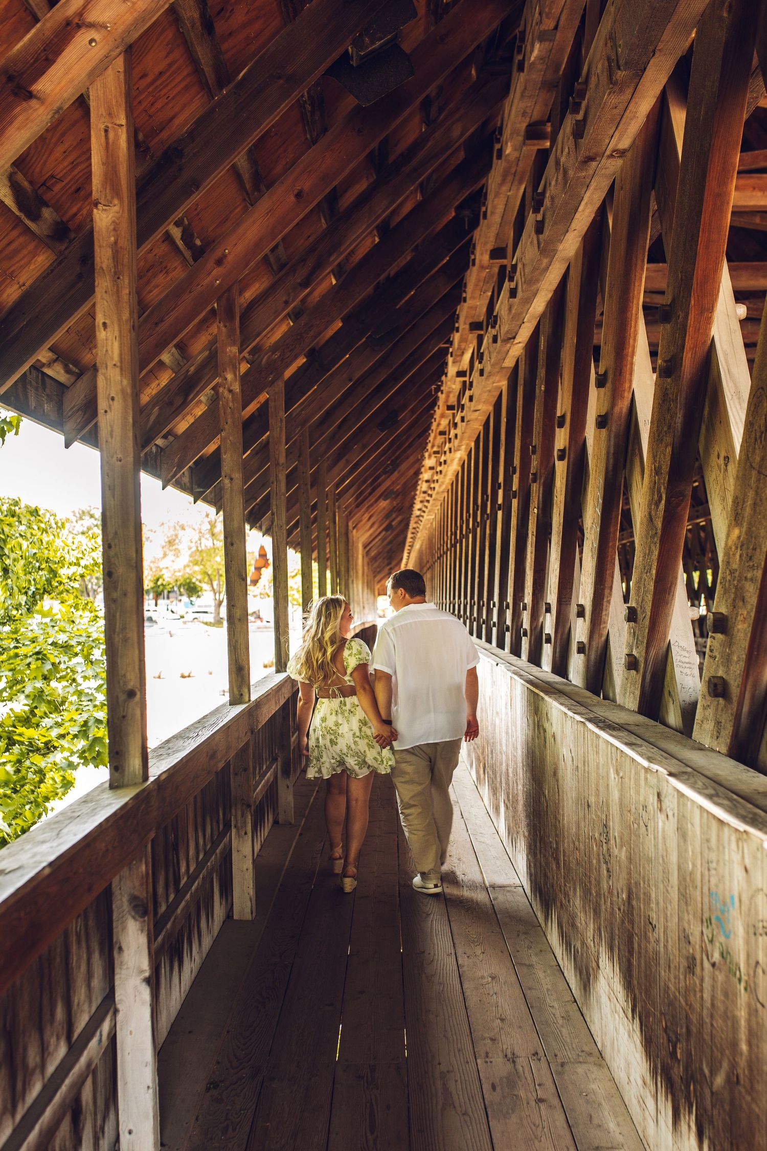 A couple walking through a rustic covered wooden bridge walkway.