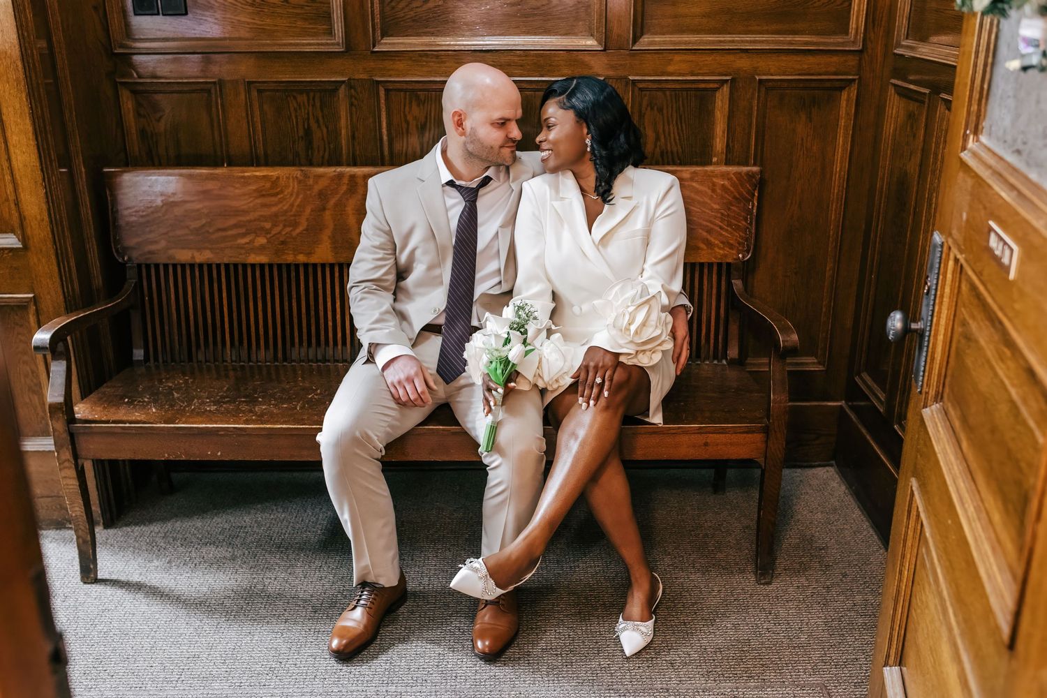 A couple sits together on a wooden bench in a warm, rustic interior hallway.