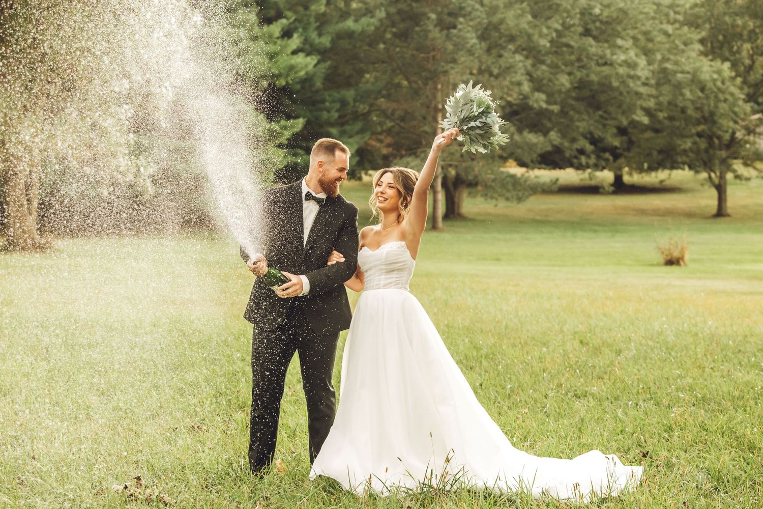 A couple in wedding attire embraces in a sunlit garden setting with natural greenery in the background.