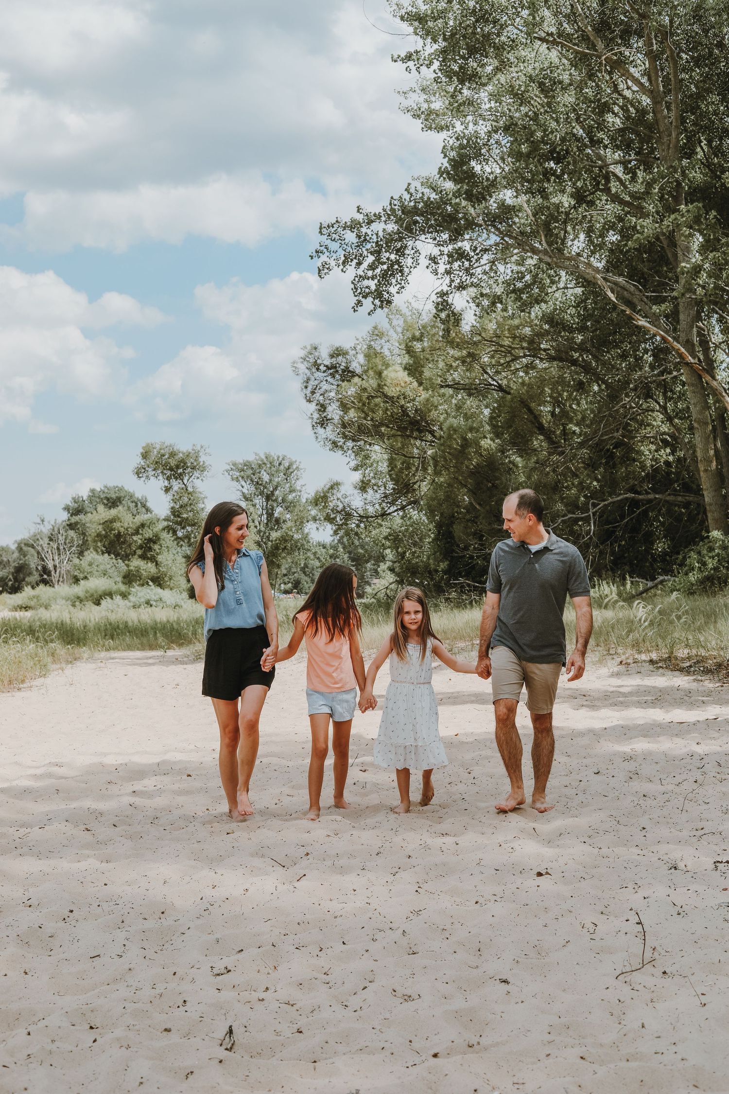Family wearing coordinated casual outfits walking together on a sandy nature trail.