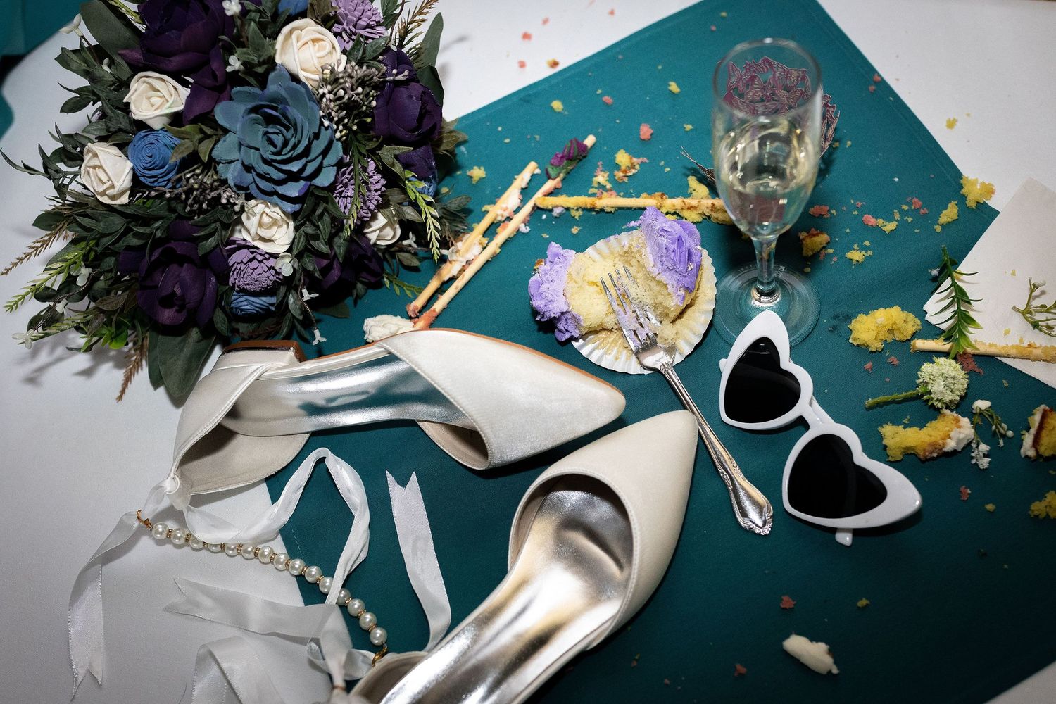 Wedding detail flatlay with flowers and decorations on a teal background.