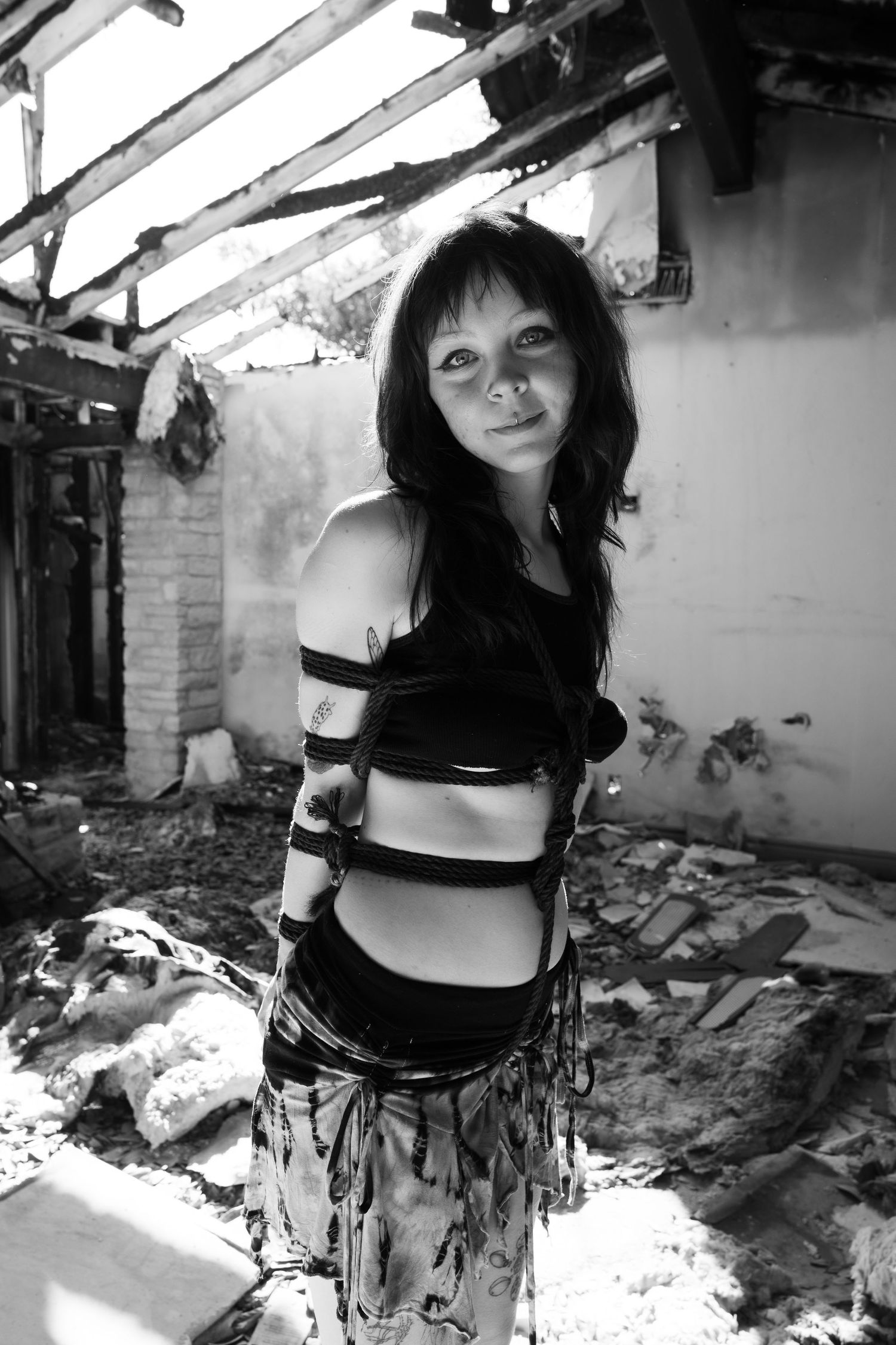 Black and white photo of woman in torn clothing standing in abandoned building.