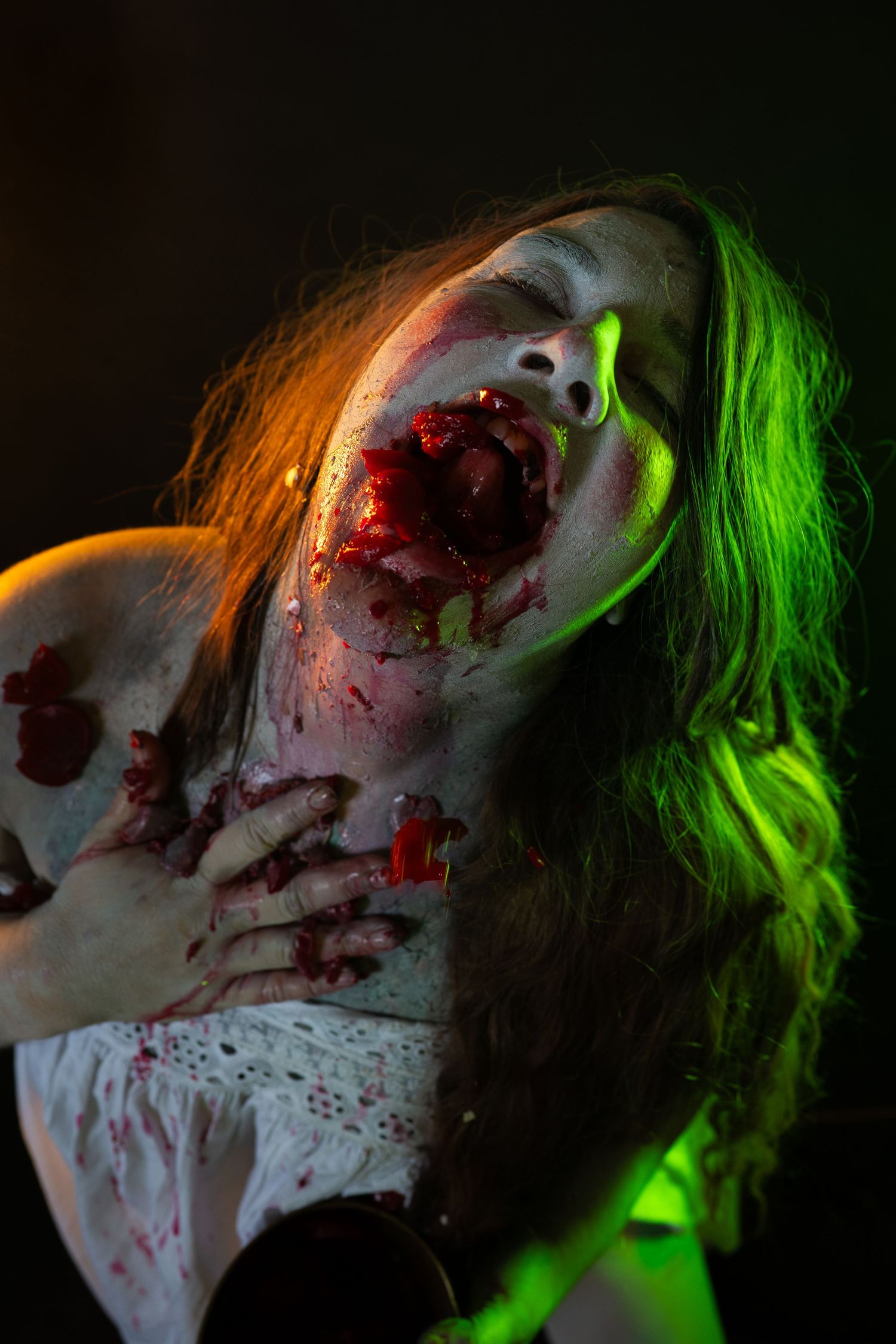 Dramatic zombie Halloween makeup with fake blood wounds and green lighting on a woman in costume.