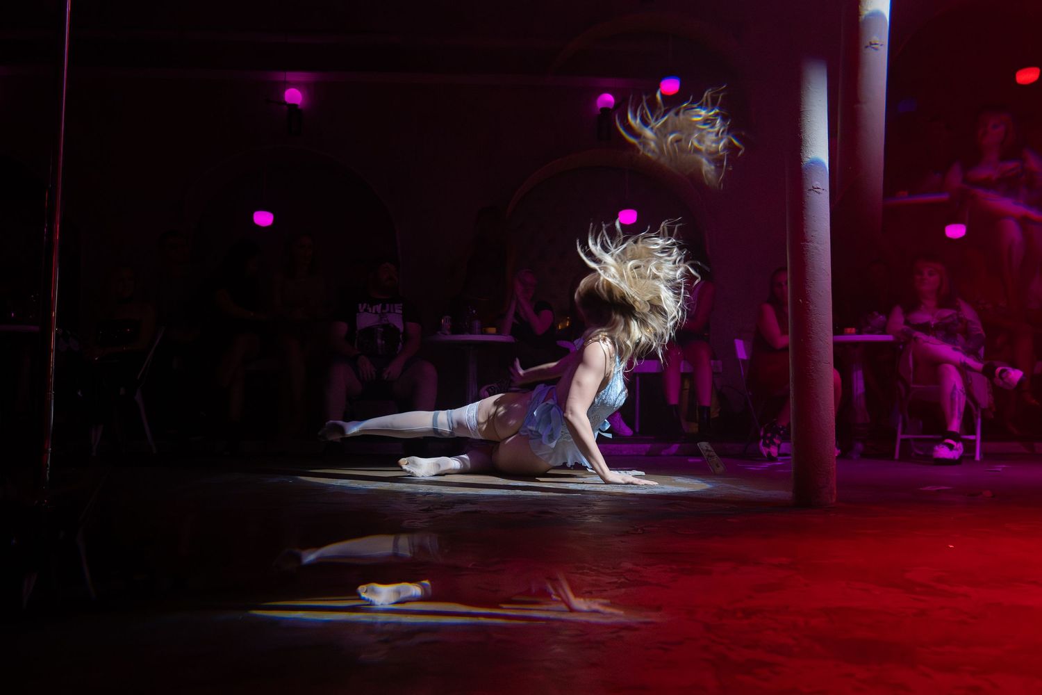 Dancer flips hair dramatically while performing a floor routine under red and purple stage lights.