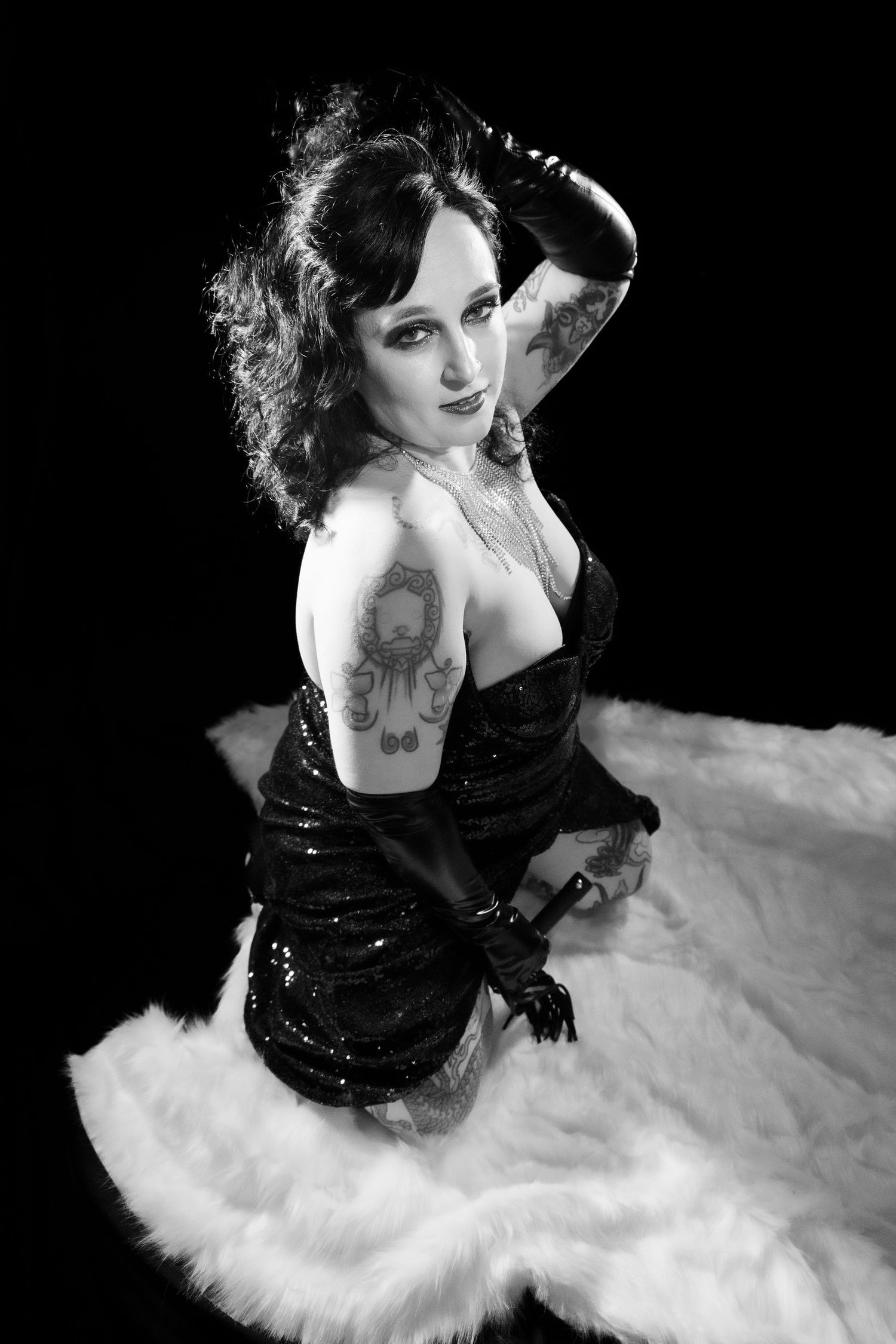 Tattooed woman in black sequin dress and gloves poses dramatically in black and white photo.
