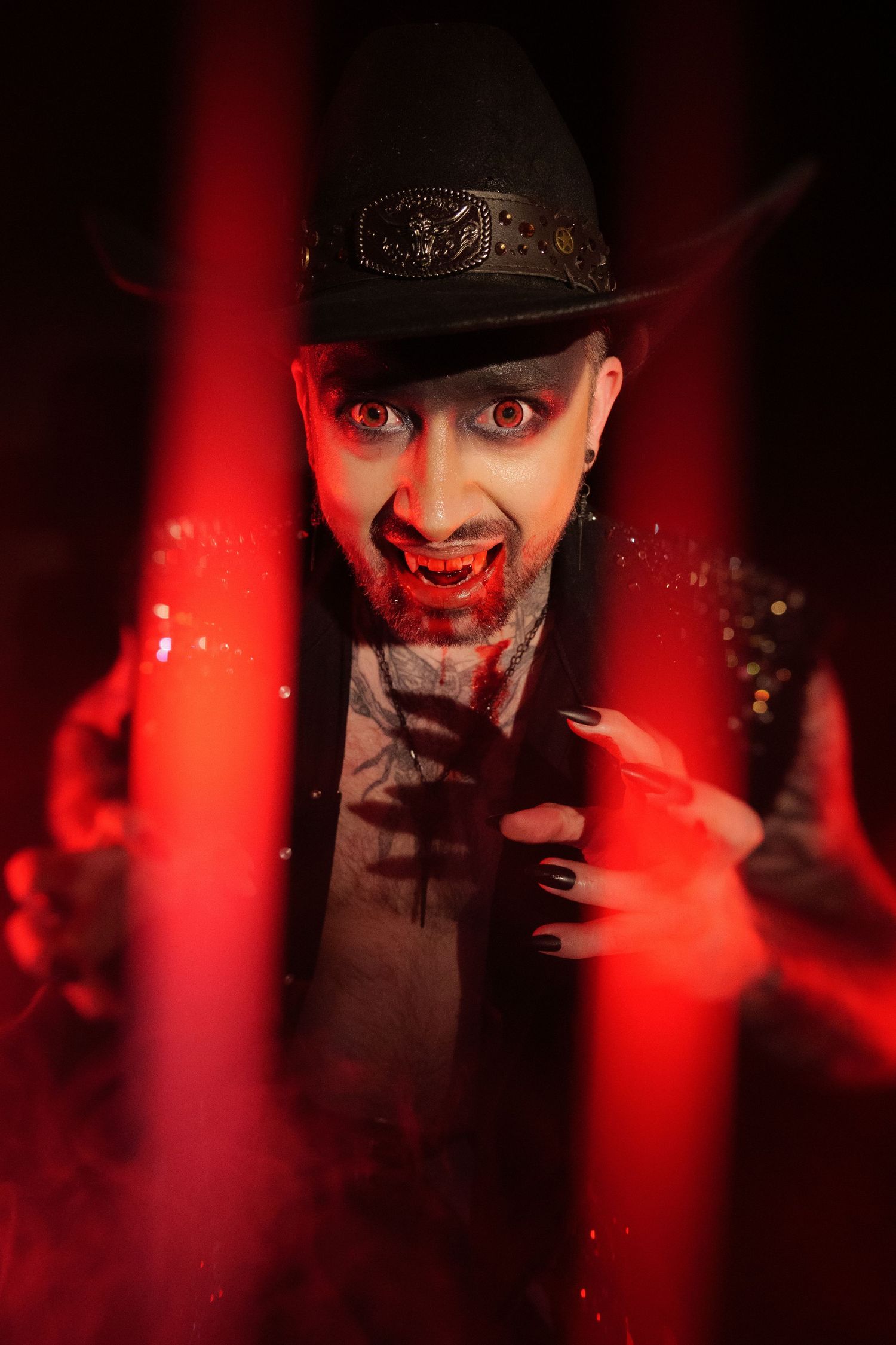 A menacing vampire costume with bloody fangs, black cowboy hat, and dramatic red lighting for Halloween.