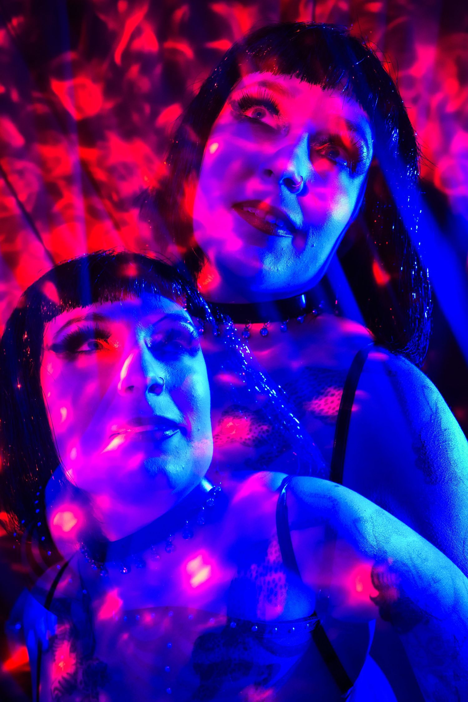 Two women illuminated by blue and red neon lights in an artistic nightclub photography setting.