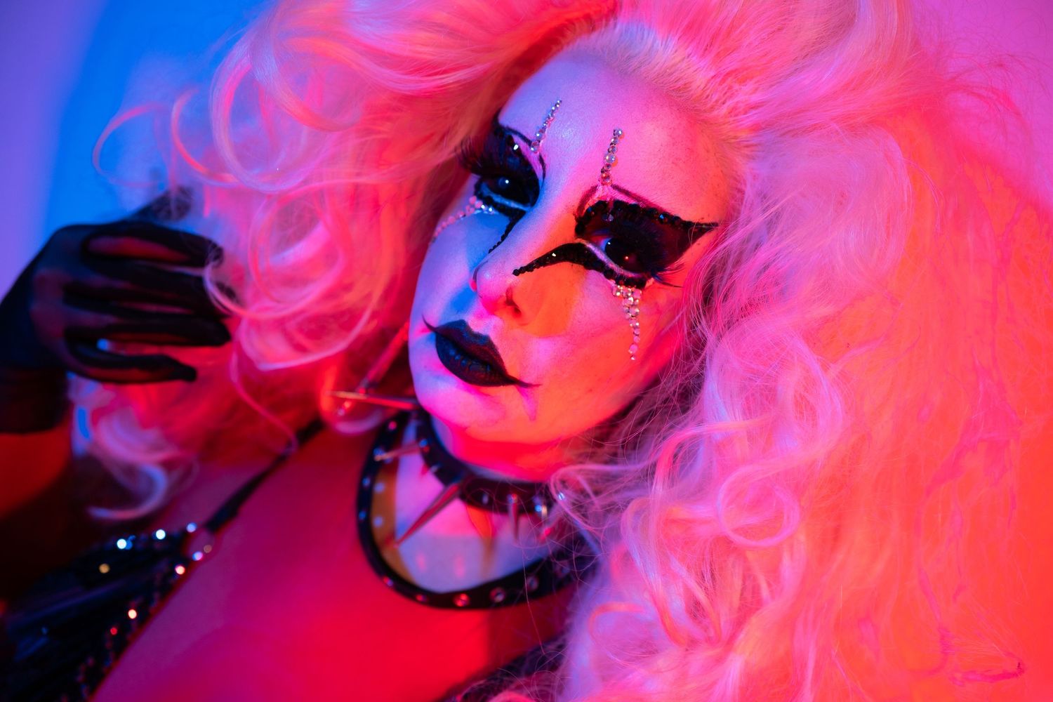 Drag performer with pink hair and dramatic skull face makeup under neon lights.
