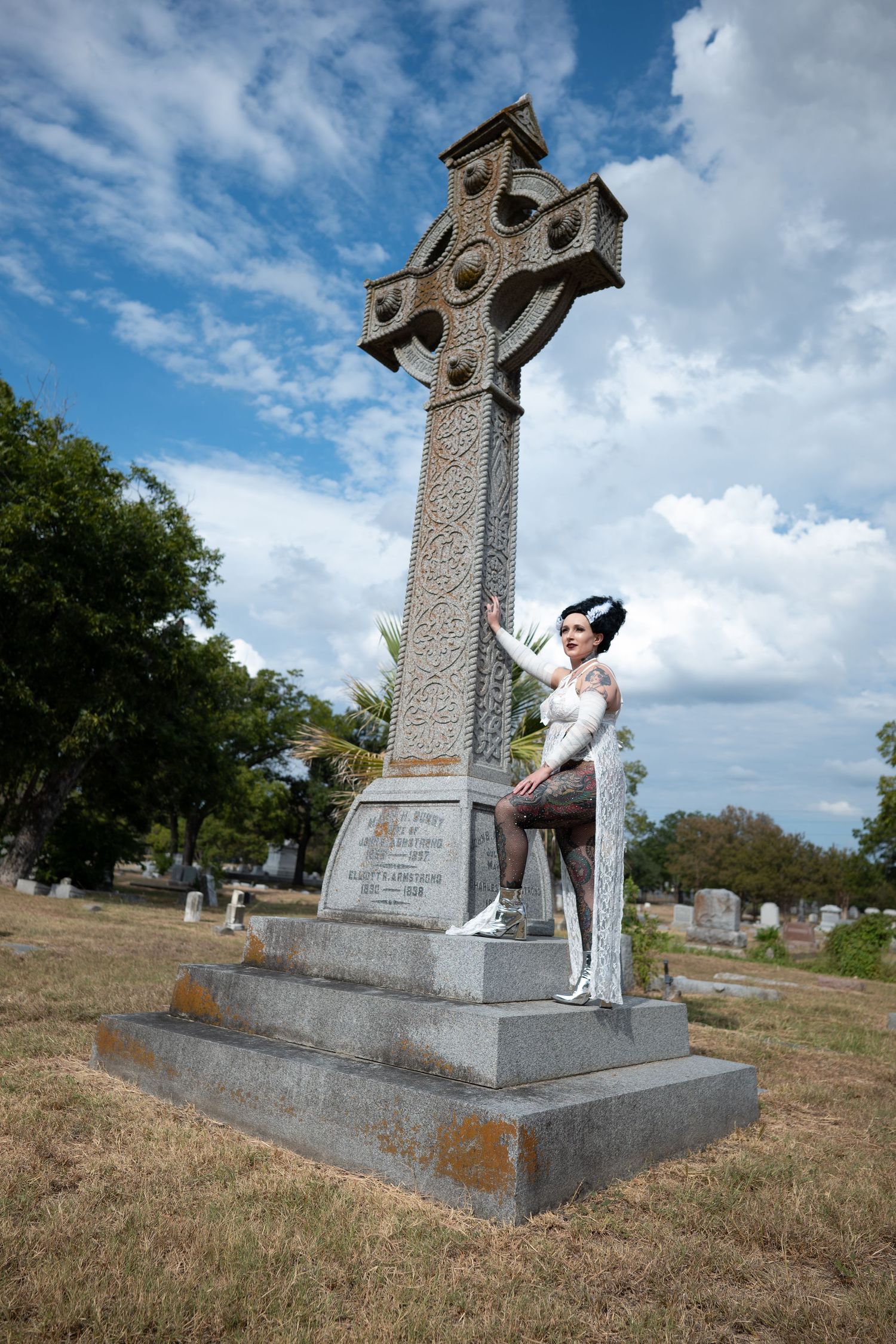 Woman in white gown leaning against tall Celtic cross monument.