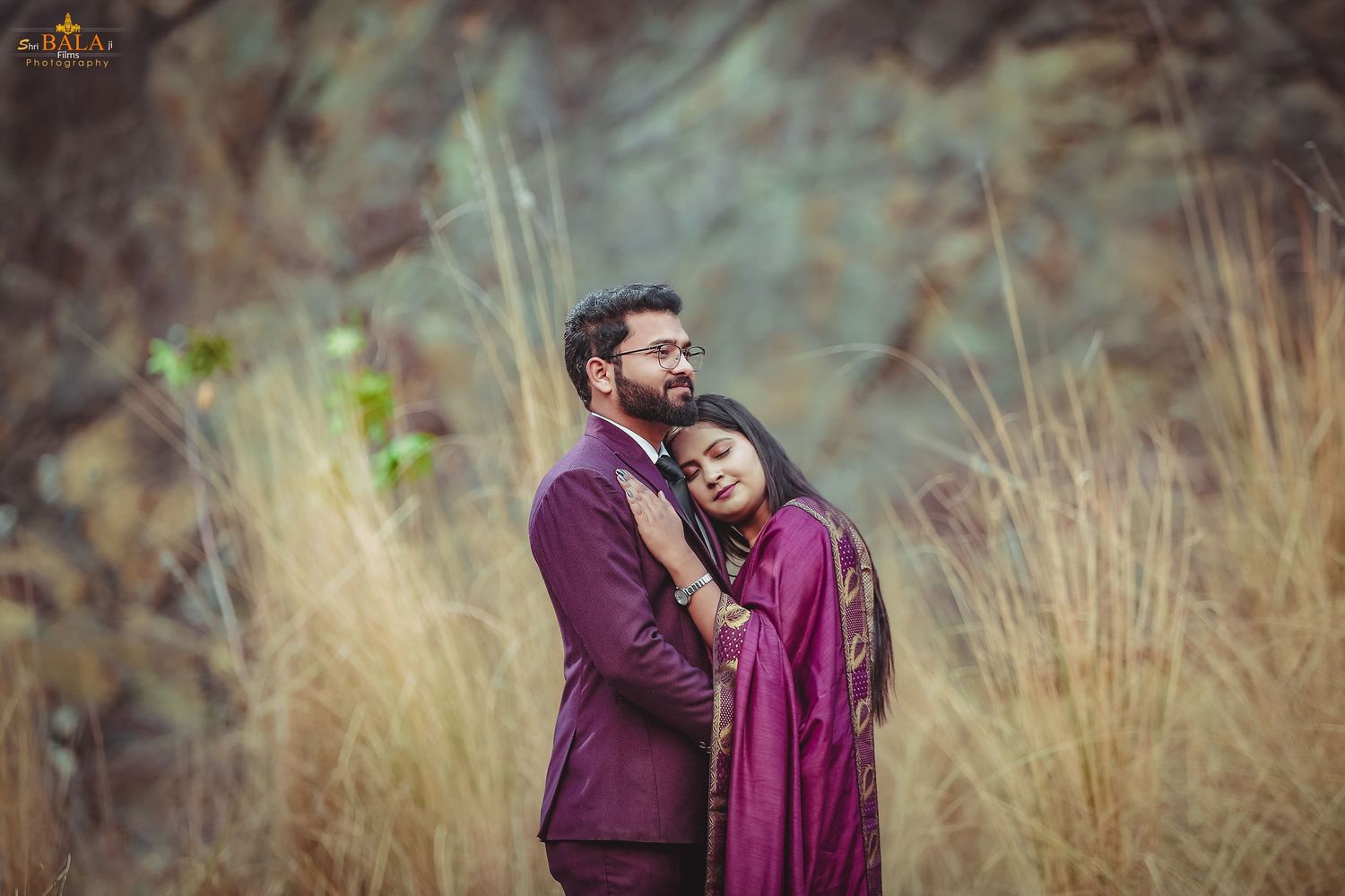 Romantic couple embracing in burgundy attire against a natural outdoor setting.