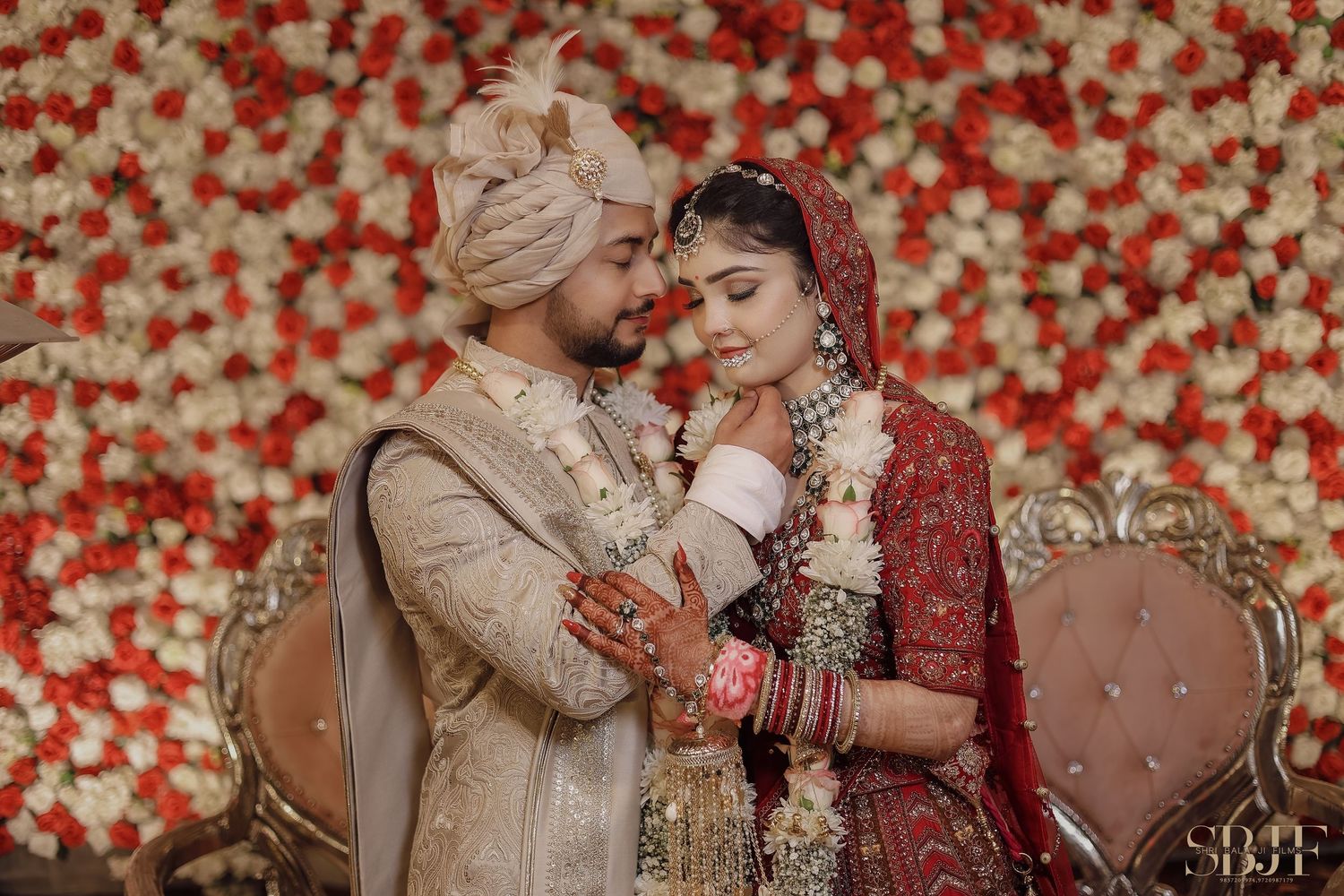 Traditional Indian wedding couple poses against a backdrop of vibrant red roses in an elegant setting.
