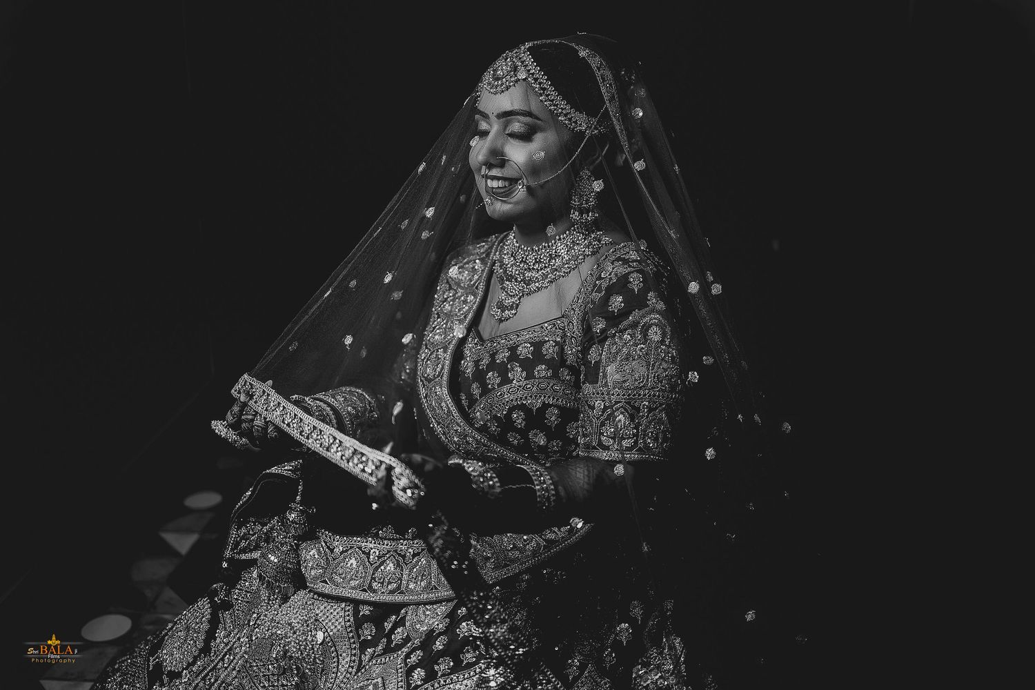 Black and white portrait of a bride in traditional Indian wedding attire with ornate jewelry and veil.