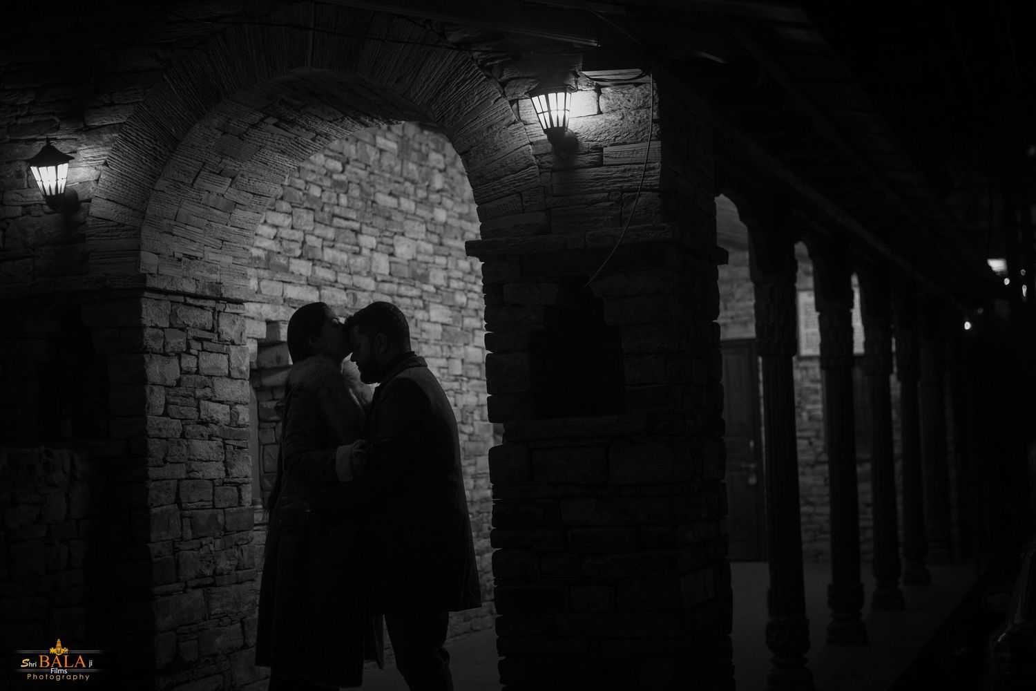 Silhouette of a couple sharing an intimate moment under a stone archway at night.