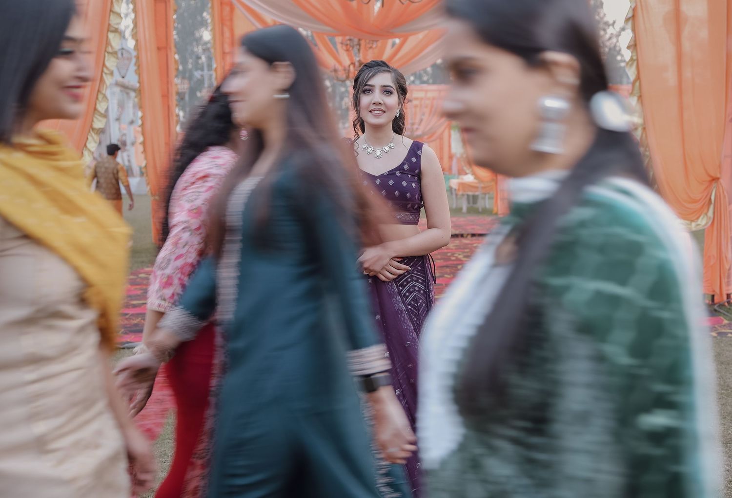 Motion blur captures women in traditional Indian clothing walking past an orange wall.