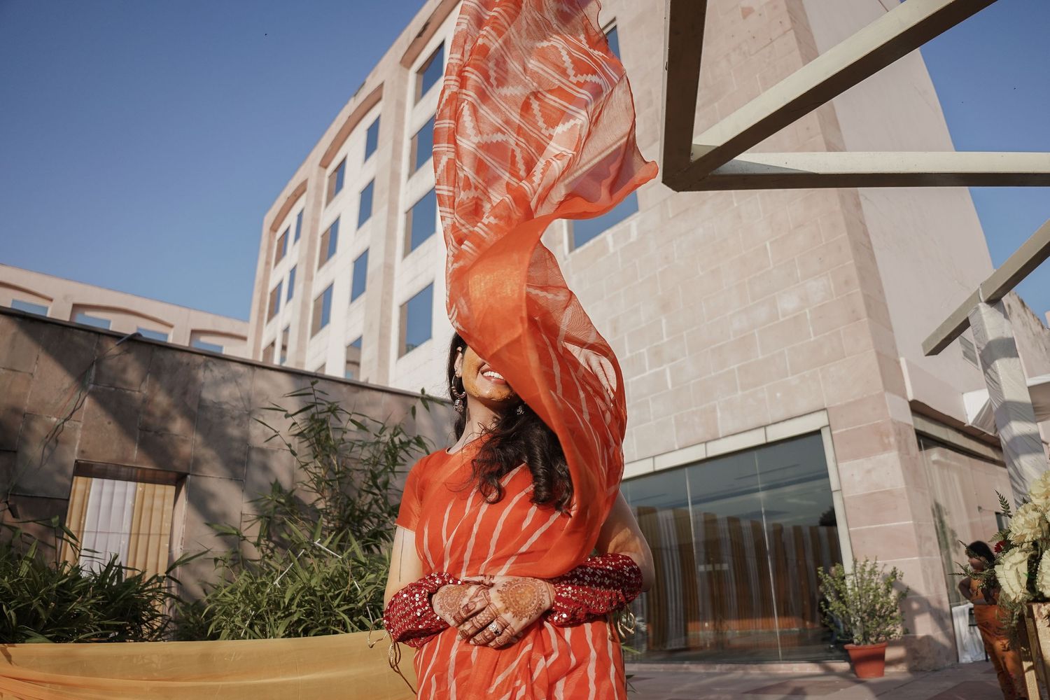 Person in flowing orange dress poses dramatically against modern architectural backdrop.