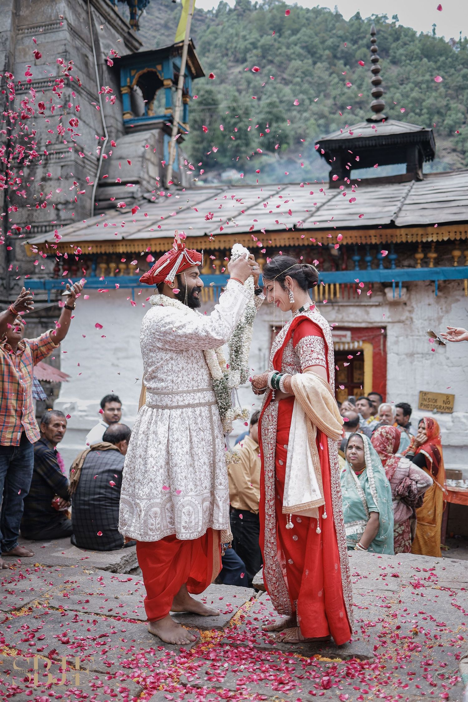 Indian bride and groom exchange garlands at traditional Hindu wedding ceremony with rose petals falling.