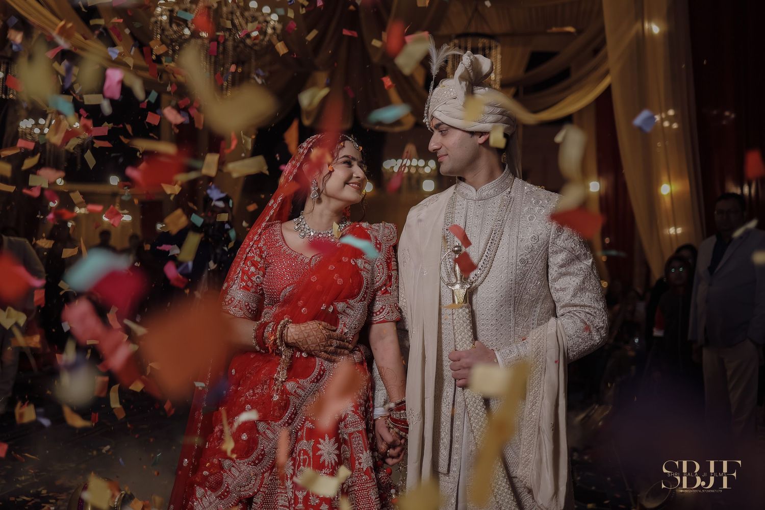 Traditional Indian wedding ceremony with confetti falling around a couple wearing red and white formal attire.