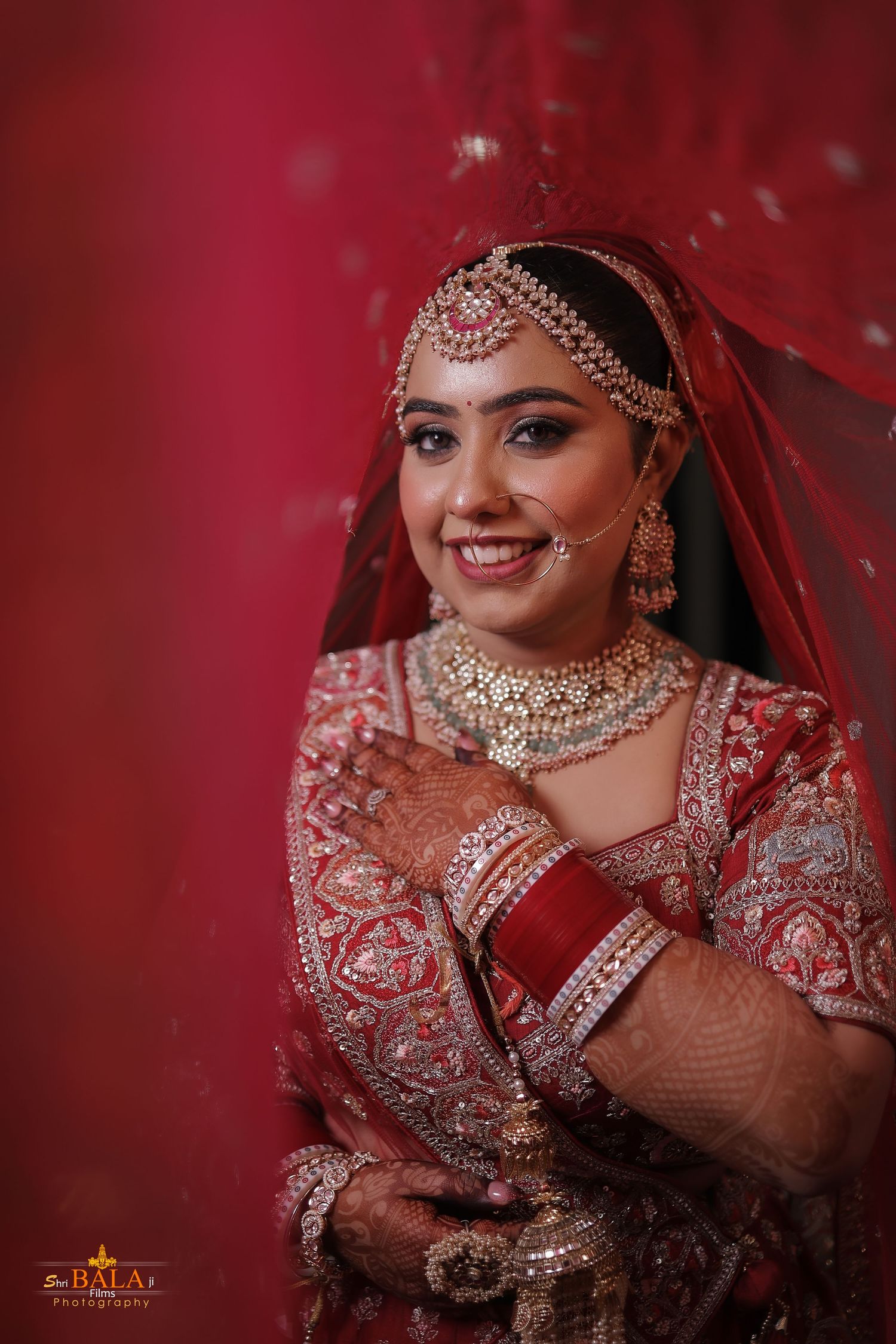 Bride in ornate red lehenga with detailed embroidery and traditional Indian bridal jewelry.