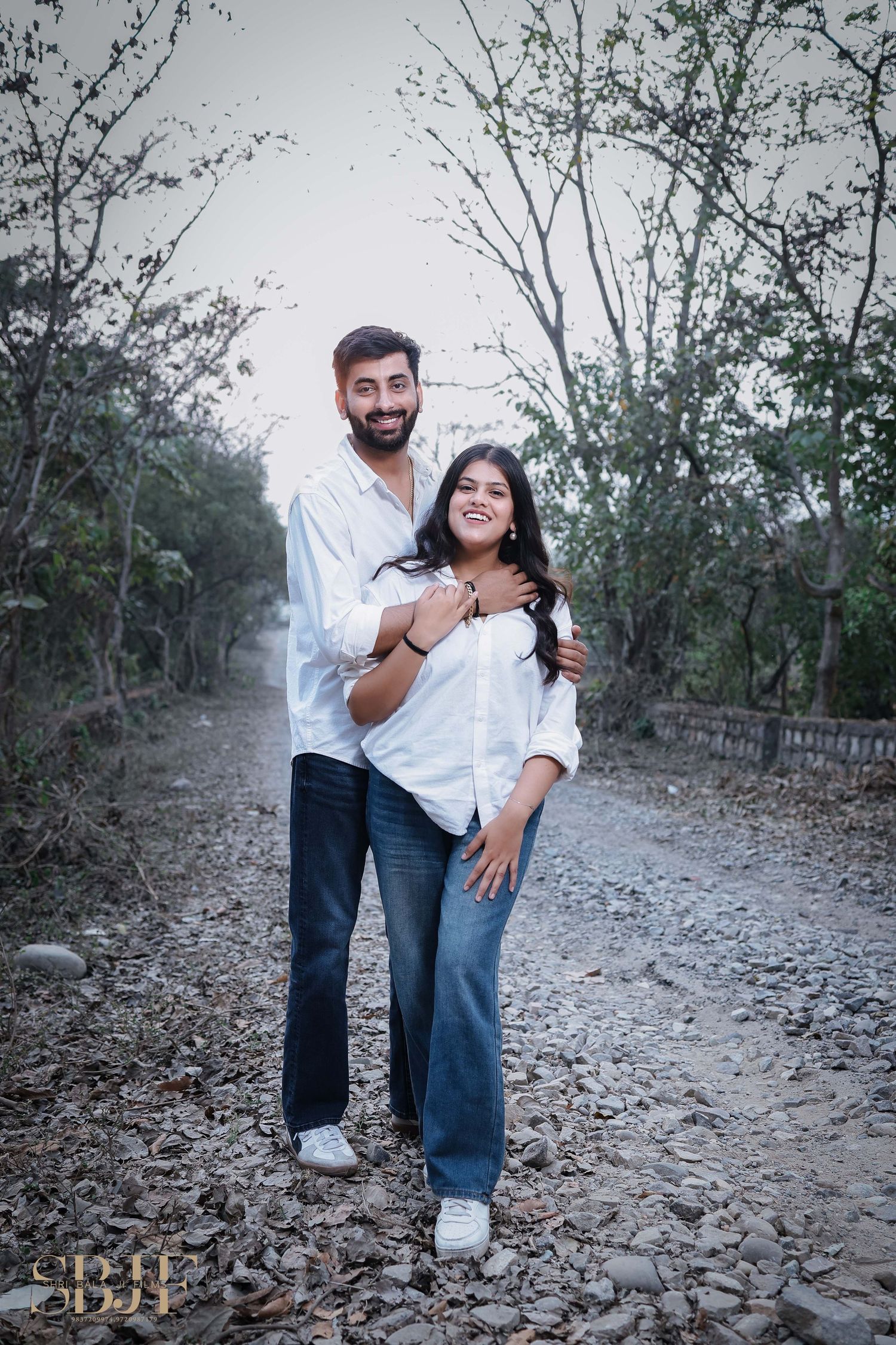 A couple shares a tender moment while walking along a rocky nature path surrounded by trees and brush.