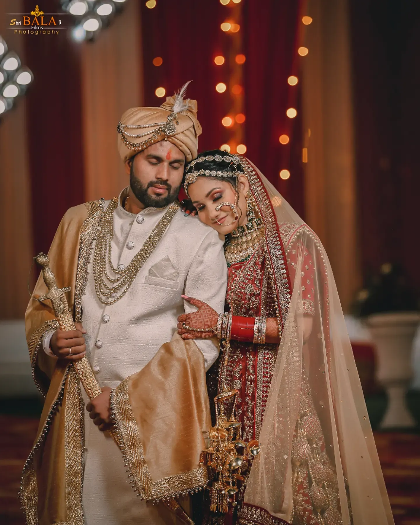 Traditional Indian wedding couple in ornate outfits with bokeh lights in background.