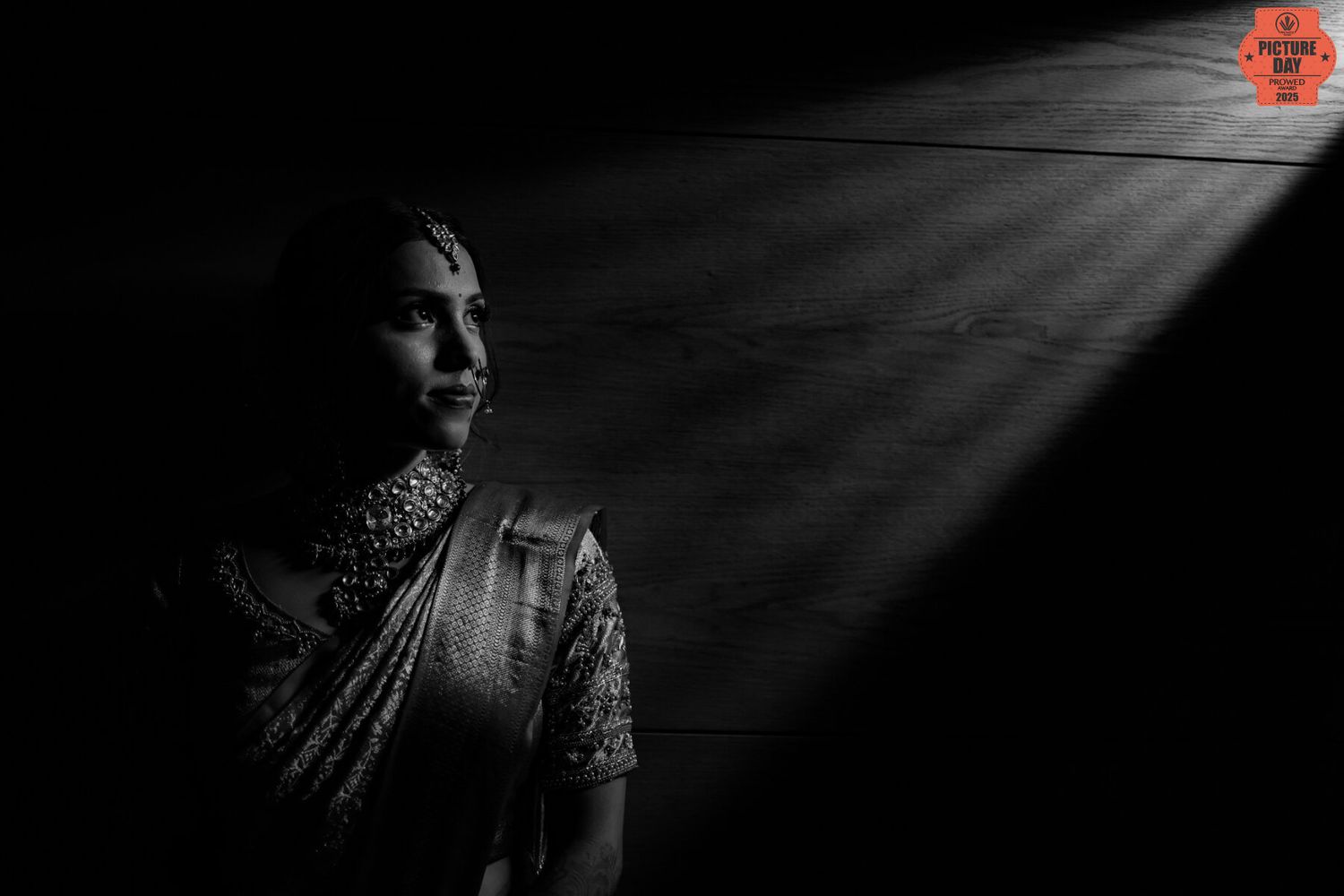 Black and white portrait of a woman in a saree with dramatic light rays in dark background.