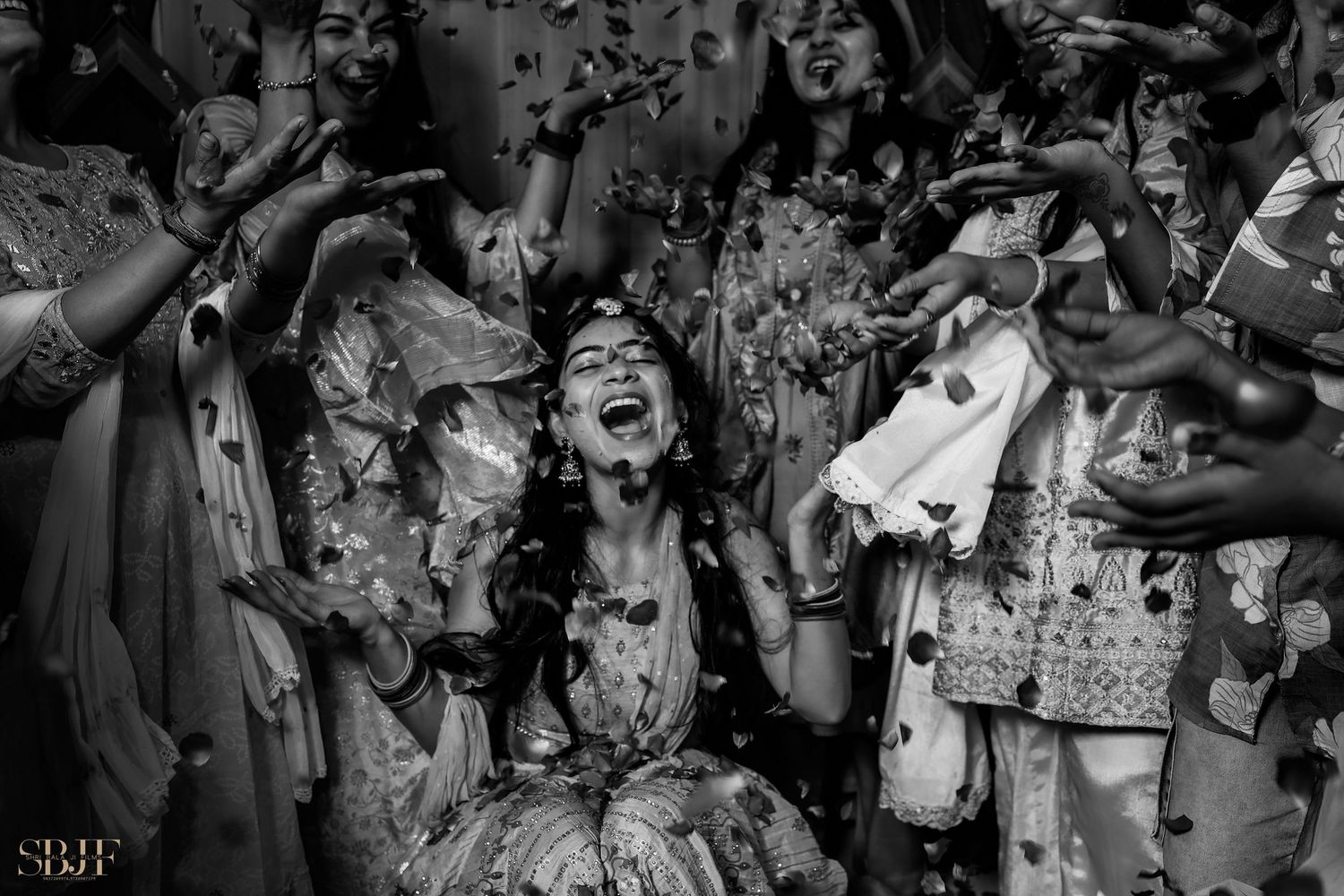 Black and white photo of a joyful bride laughing as flower petals are tossed during an Indian wedding celebration.
