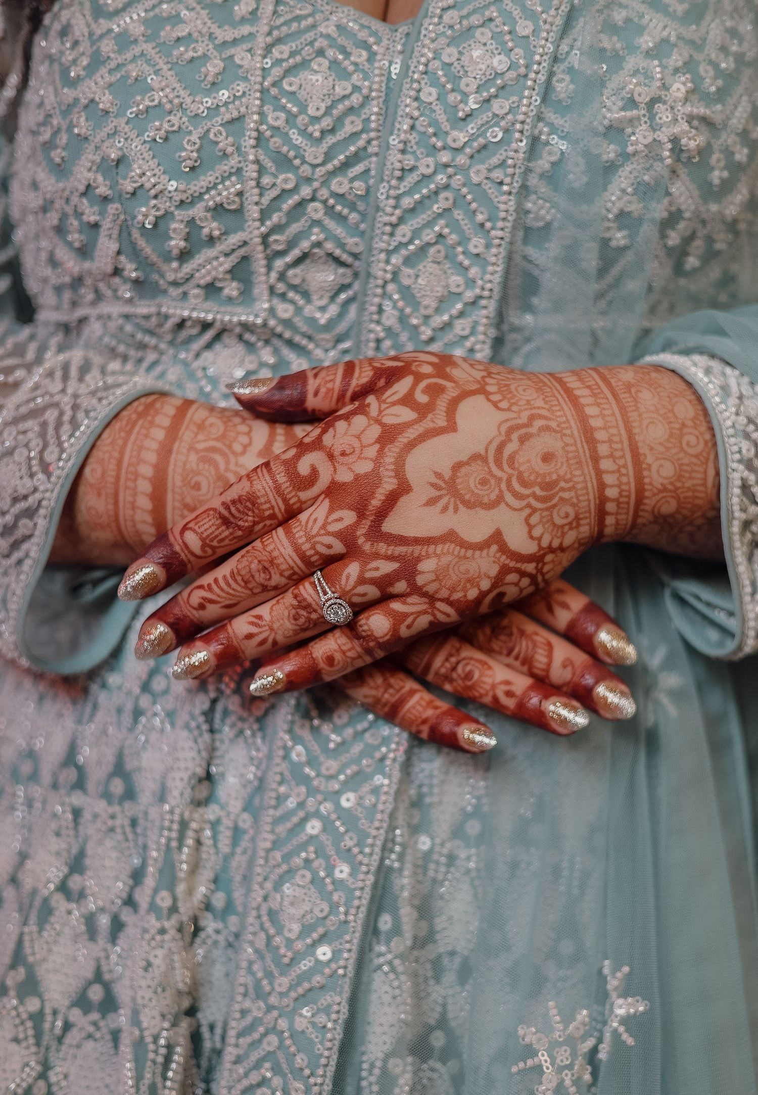 Close-up view of intricate henna designs on hands resting against a light blue embroidered fabric background.