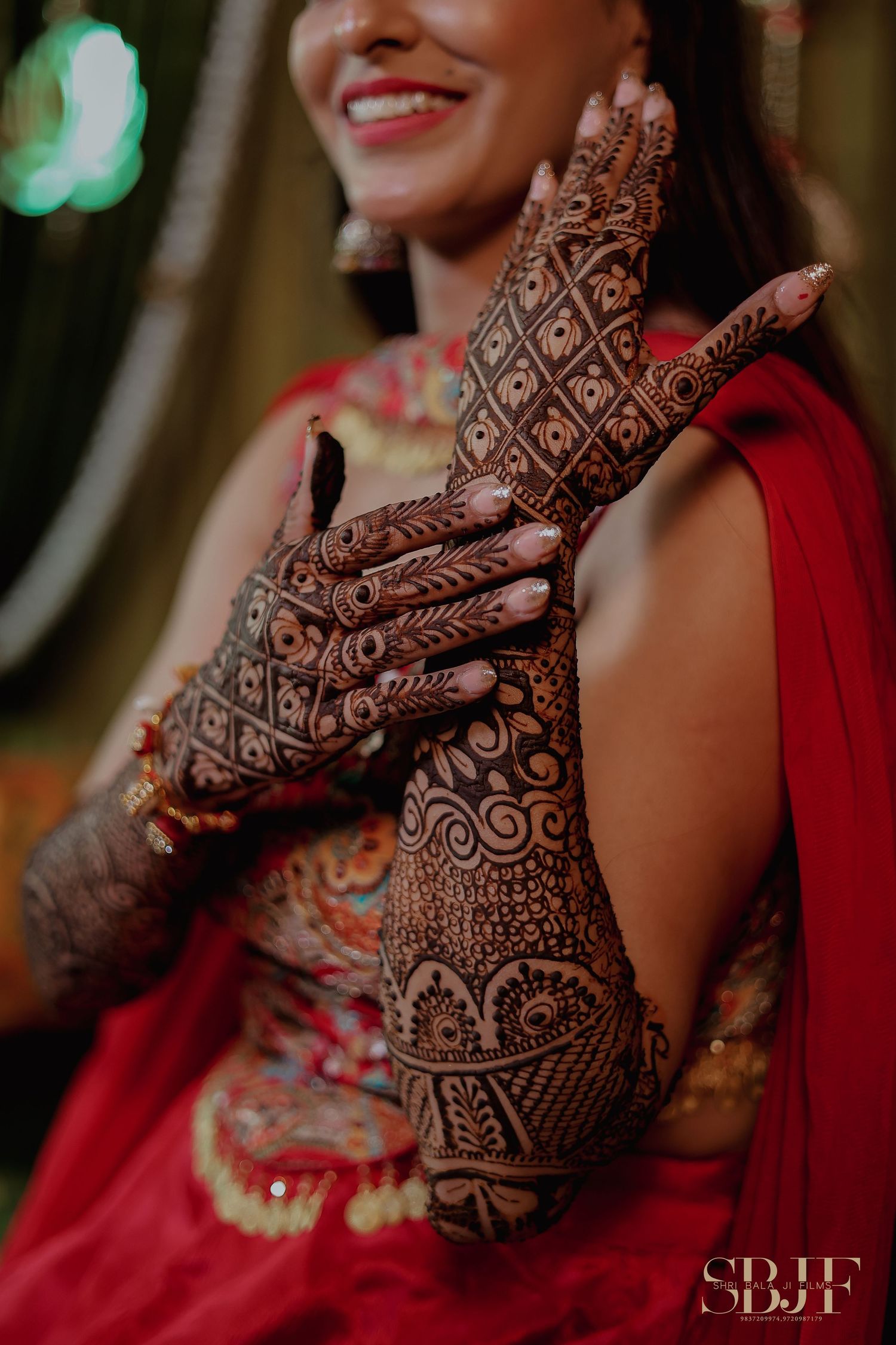 Close-up of beautifully detailed henna mehndi design on hands with red traditional clothing in the background.