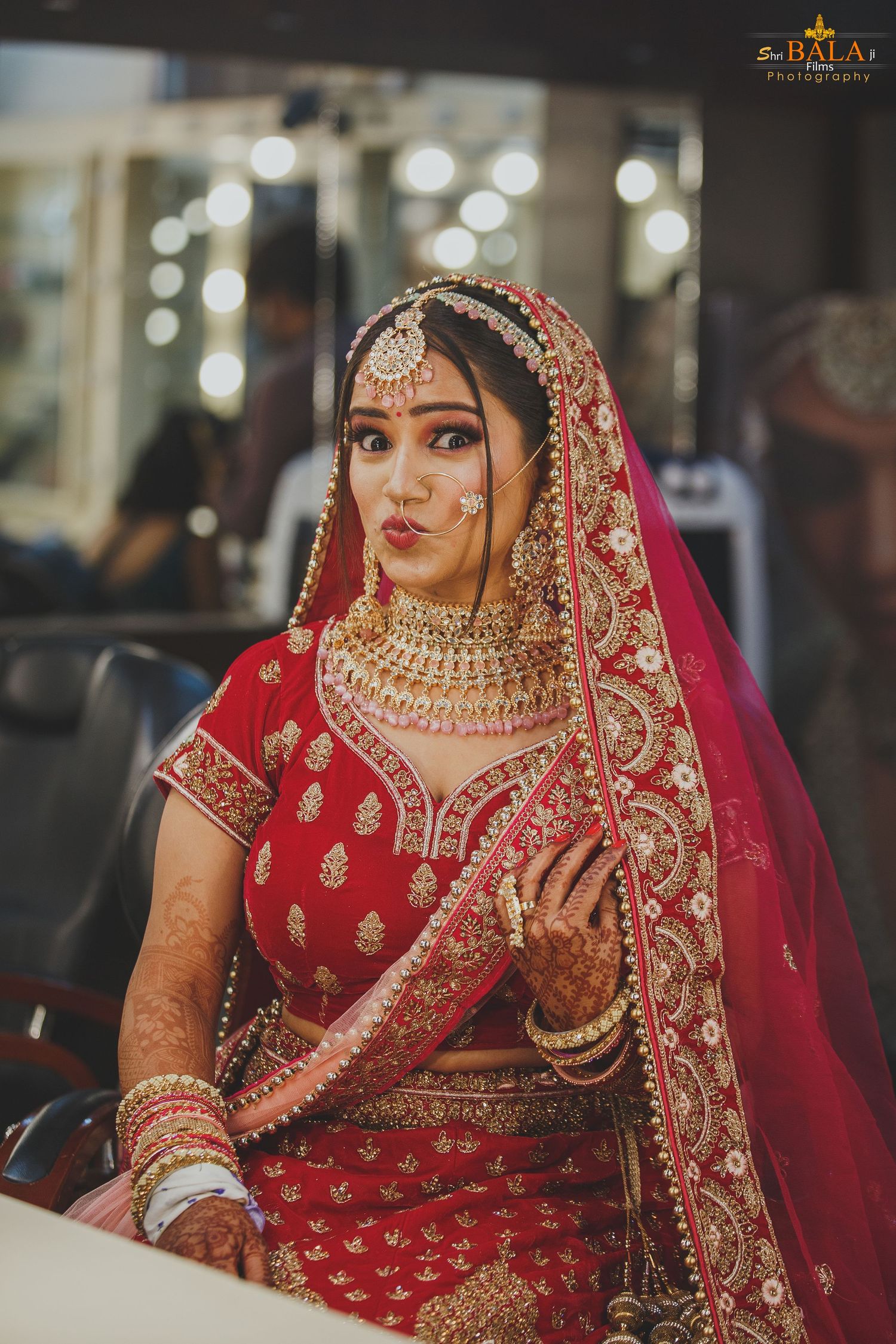 Indian bride in red bridal lehenga with heavy gold jewelry and traditional makeup.