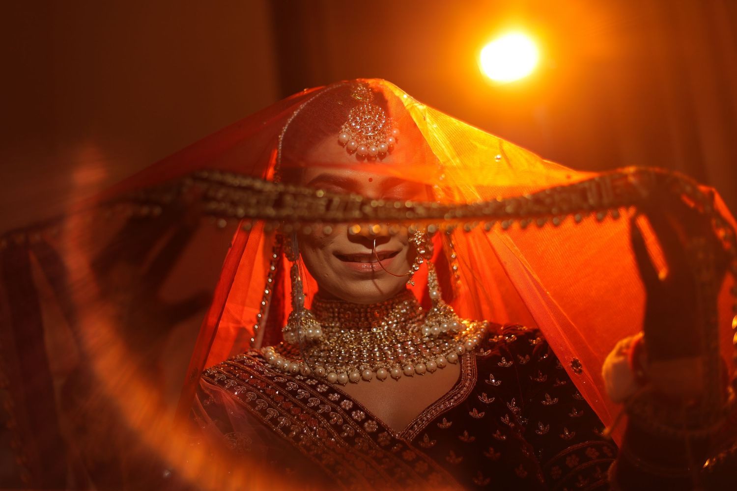 Traditional Indian bridal portrait with dramatic lighting and ornate jewelry silhouetted against a sunset.