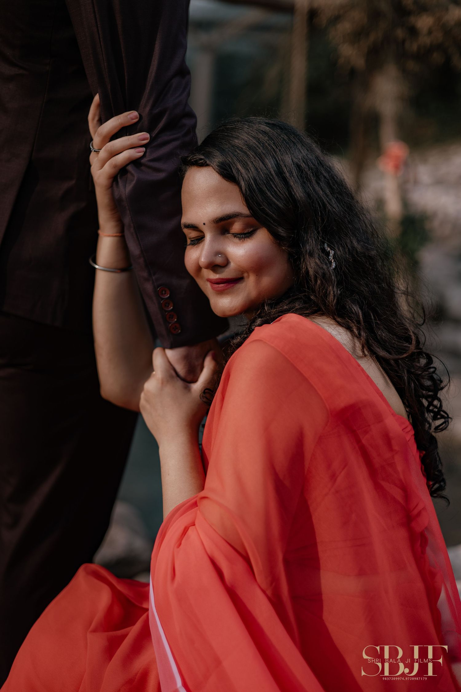 Intimate portrait of person in coral dress holding companion's arm outdoors.