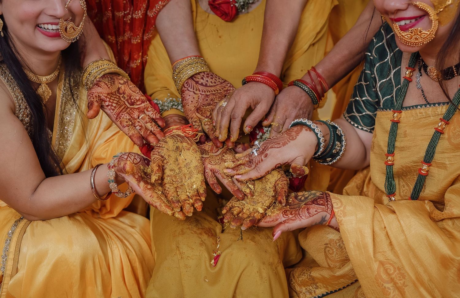 Close-up view of hands adorned with traditional Indian bridal jewelry and henna designs against yellow fabric.