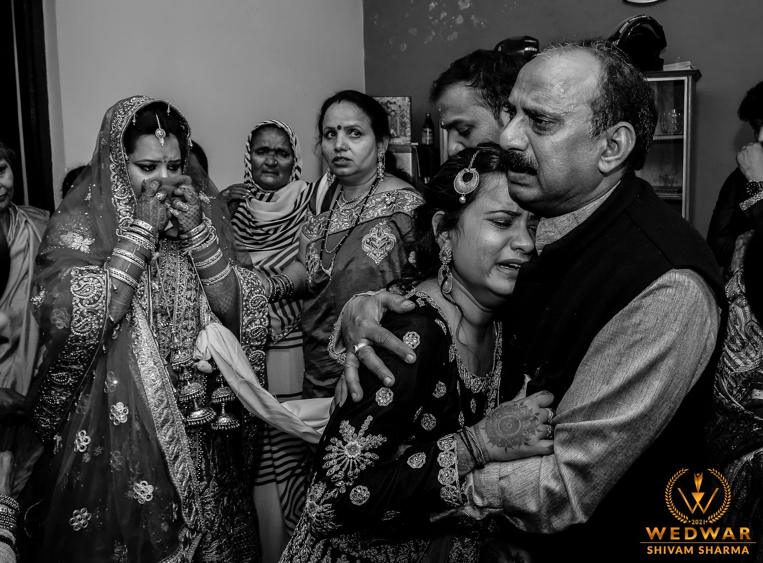 Emotional black and white wedding photo showing bride crying surrounded by family during traditional Indian farewell ceremony.