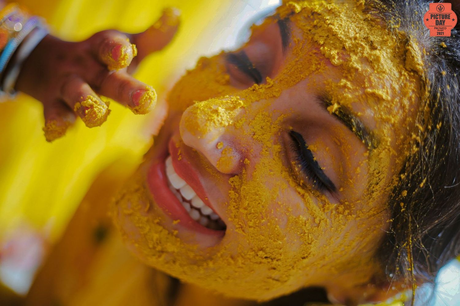 A joyful woman with her face covered in bright yellow turmeric paste during a traditional Haldi ceremony.