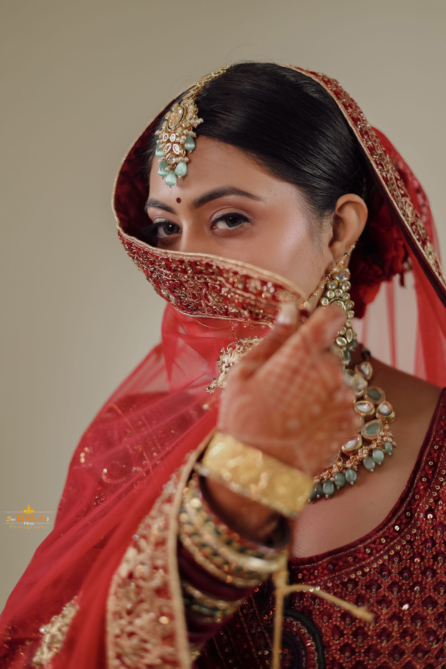 Close up of Indian bridal jewelry and red veil with intricate embroidery.