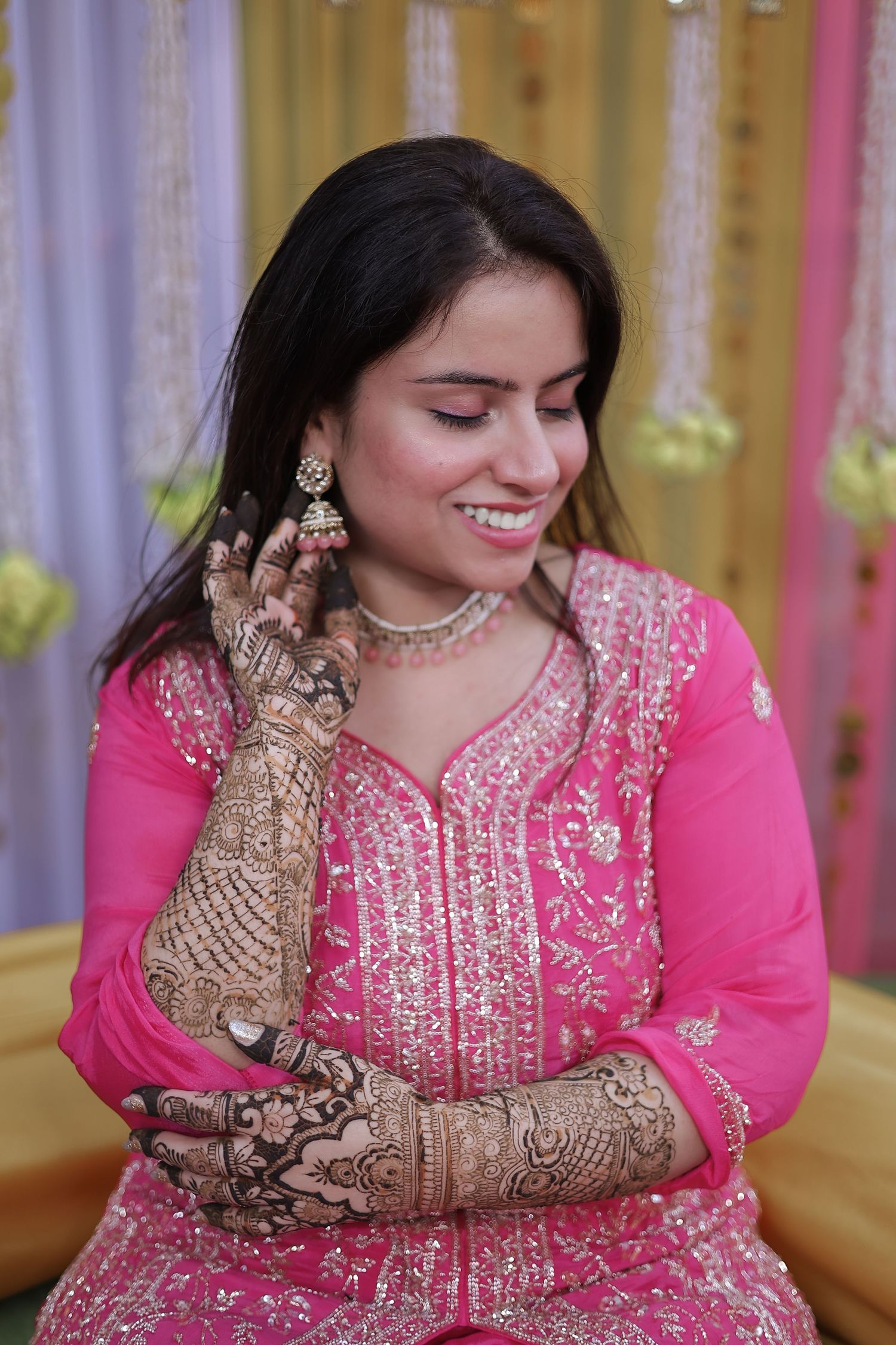 Person wearing a pink embroidered dress displays intricate henna designs on their hands while smiling.