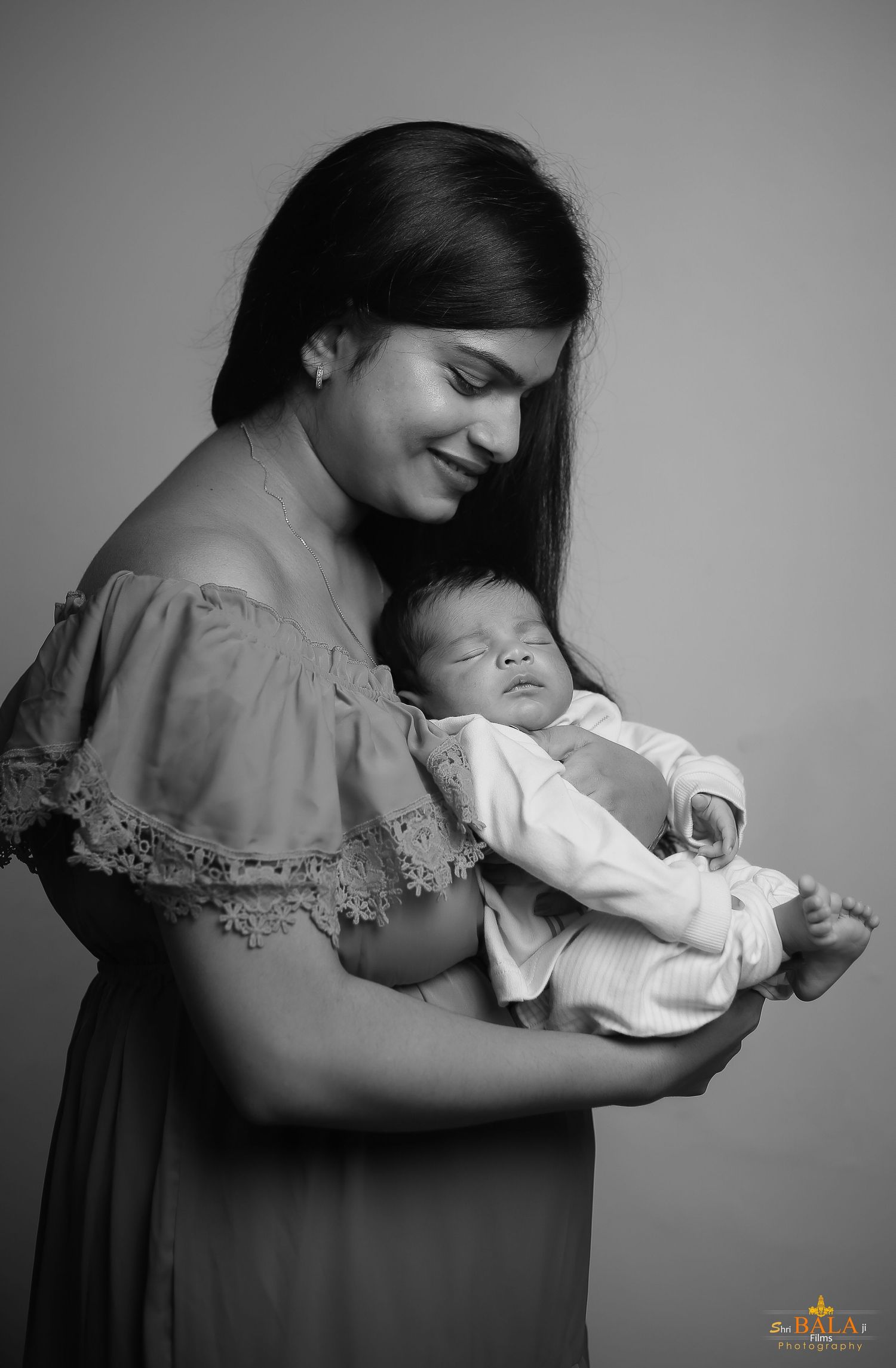 A tender black and white portrait of a mother holding her sleeping newborn.