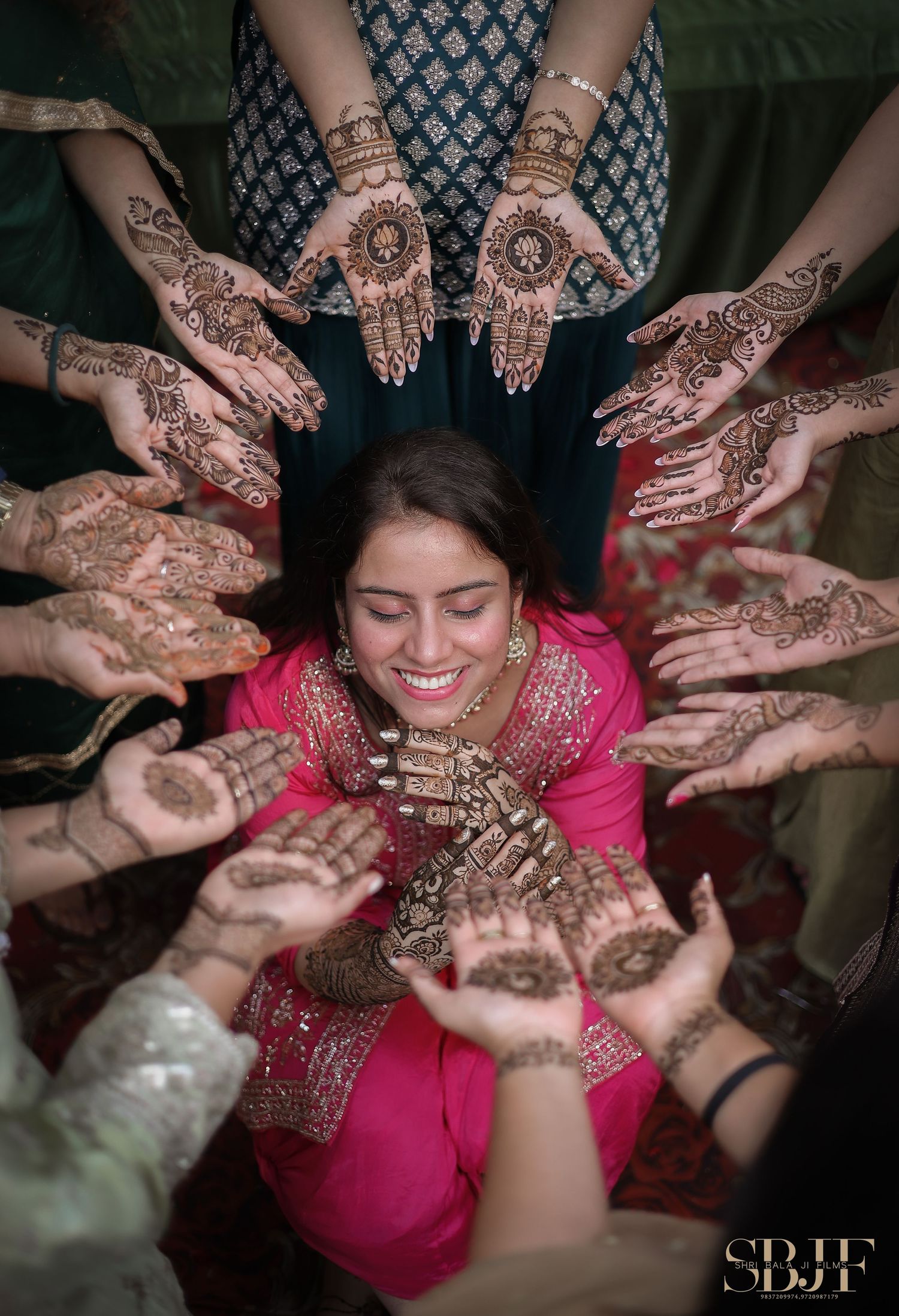 Traditional mehndi ceremony showing hands decorated with henna designs surrounding person in pink.
