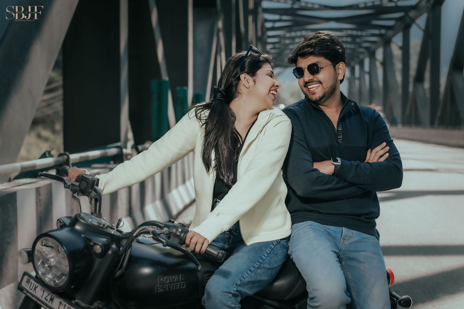 Couple sharing a romantic moment on a motorcycle on a bridge, man in sunglasses with arms crossed.