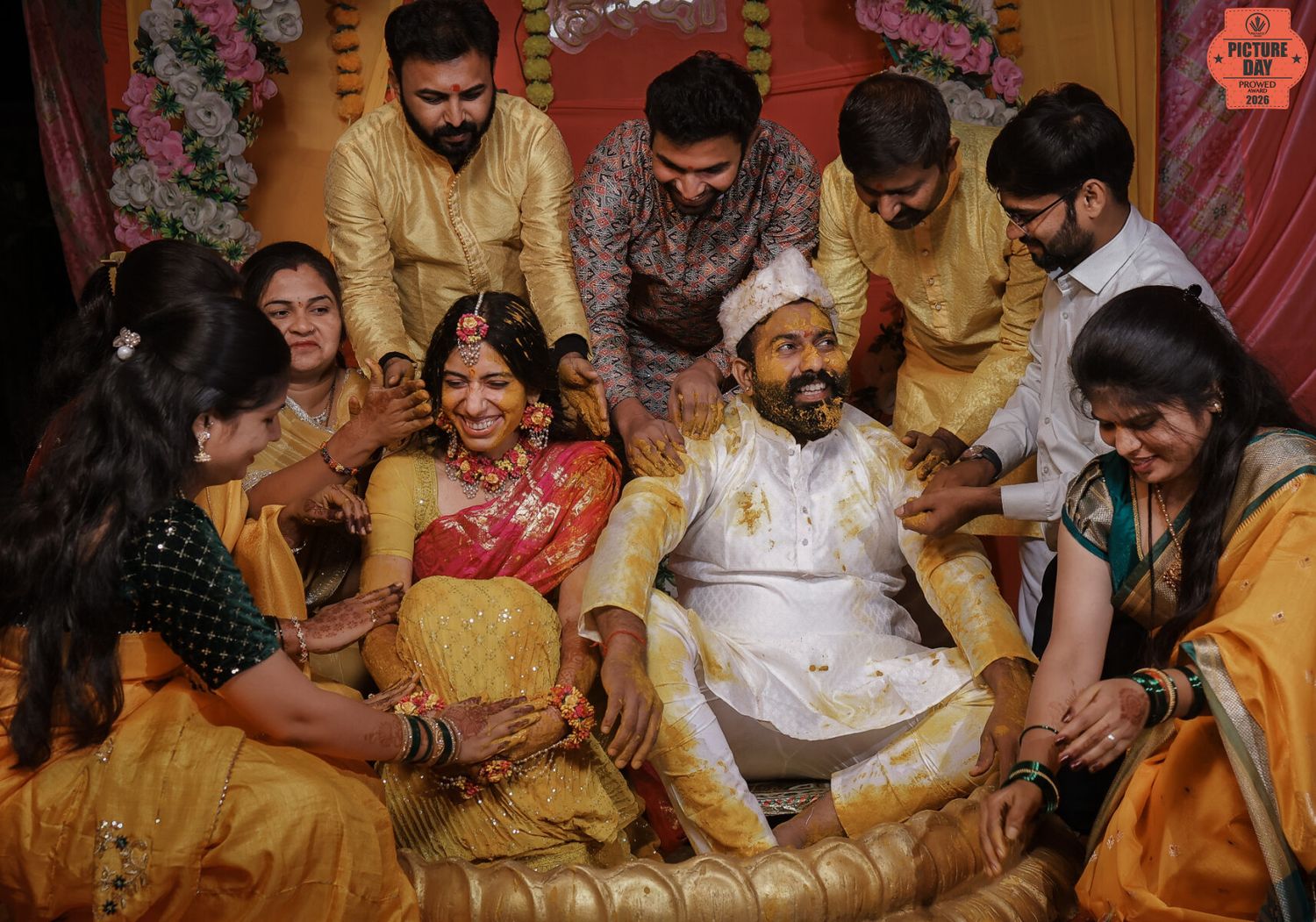 Indian wedding haldi ceremony with bride and groom surrounded by joyful family members in traditional yellow and gold attire.