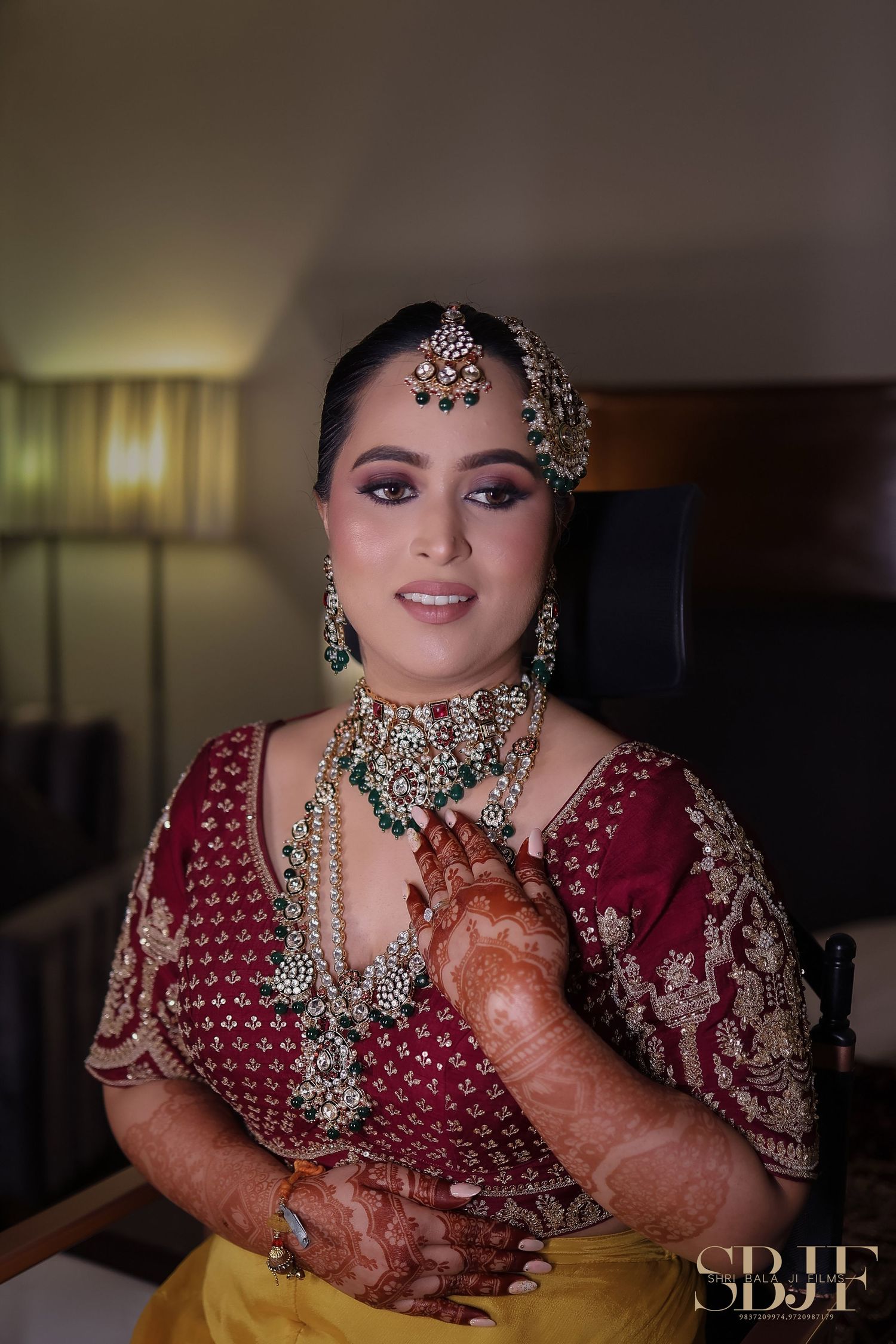 Traditional Indian bride wearing maroon embroidered lehenga with ornate jewelry and mehndi decorated hands.