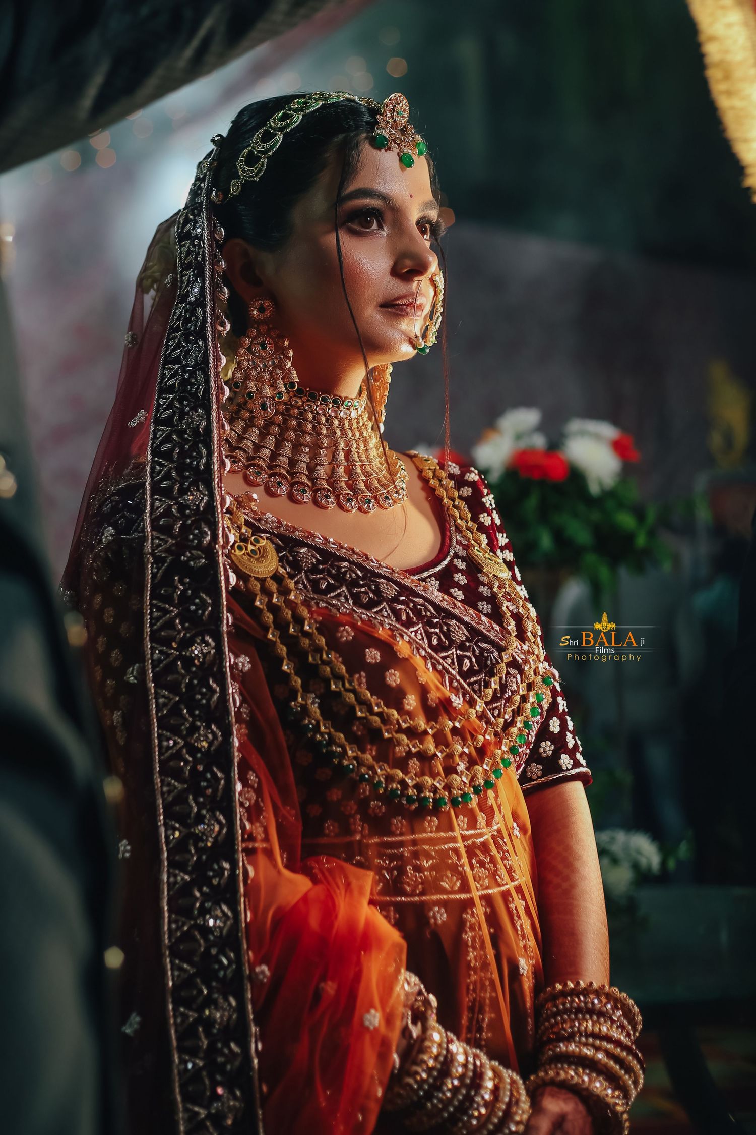 Traditional Indian bride wearing ornate gold jewelry and embroidered orange lehenga with detailed black dupatta.