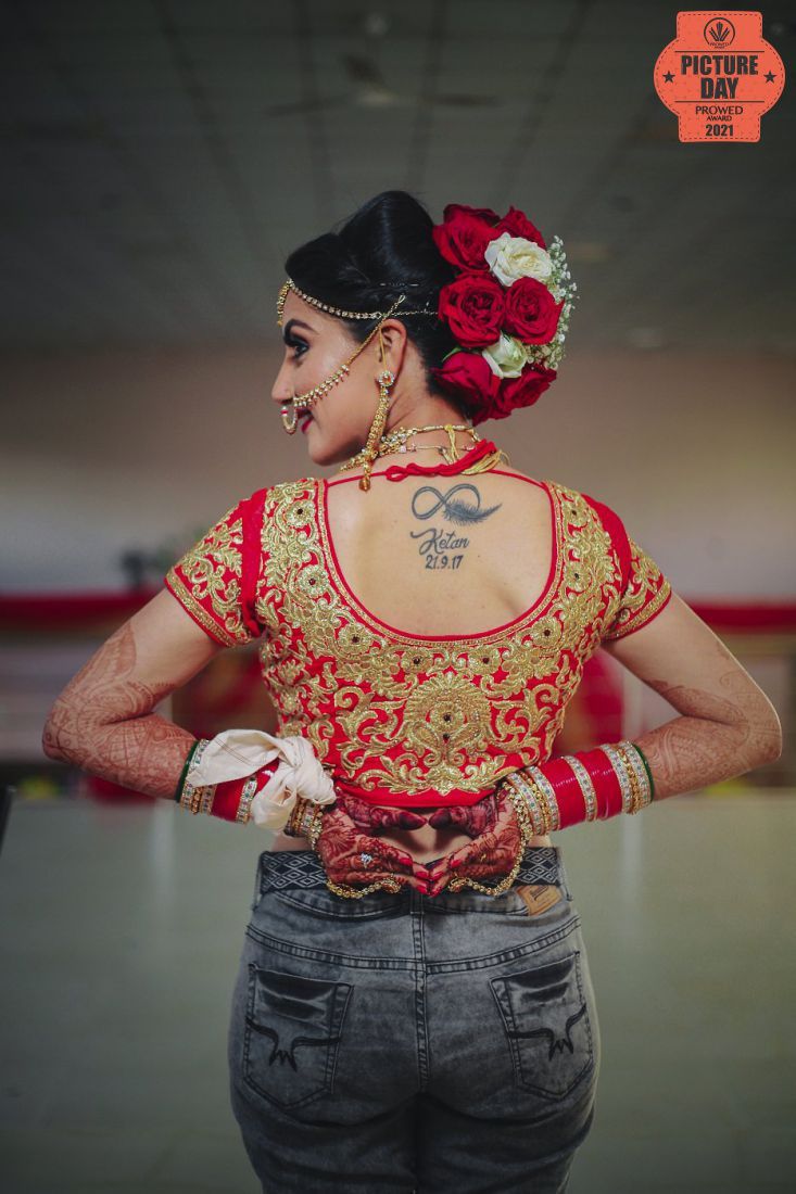 Bride in red embroidered blouse with gold detailing, floral hair accessories, and a tattoo on her back.